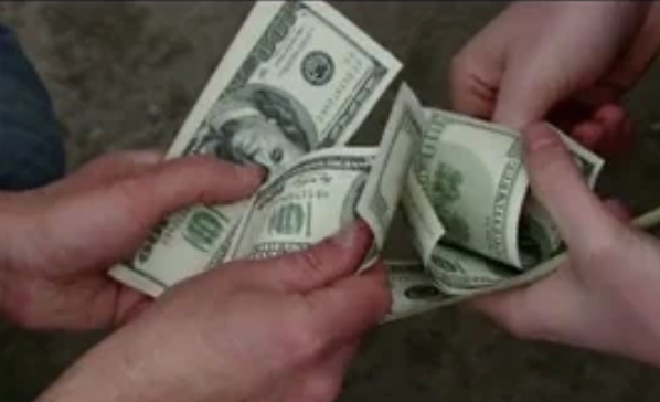 Hands exchanging several U.S. dollar bills, suggesting a transaction or exchange of money