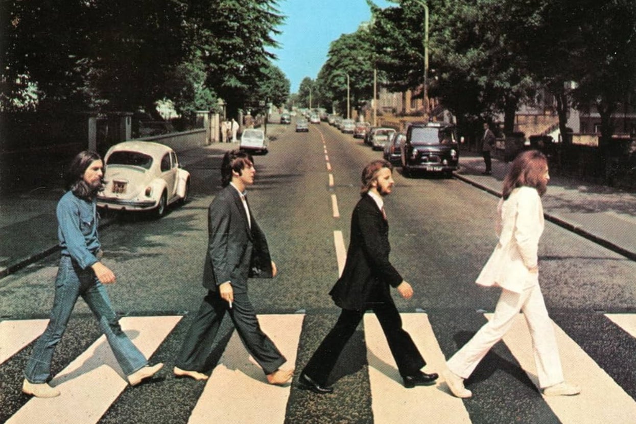 Four men in suits walk across a zebra crossing on a street, reminiscent of an iconic album cover