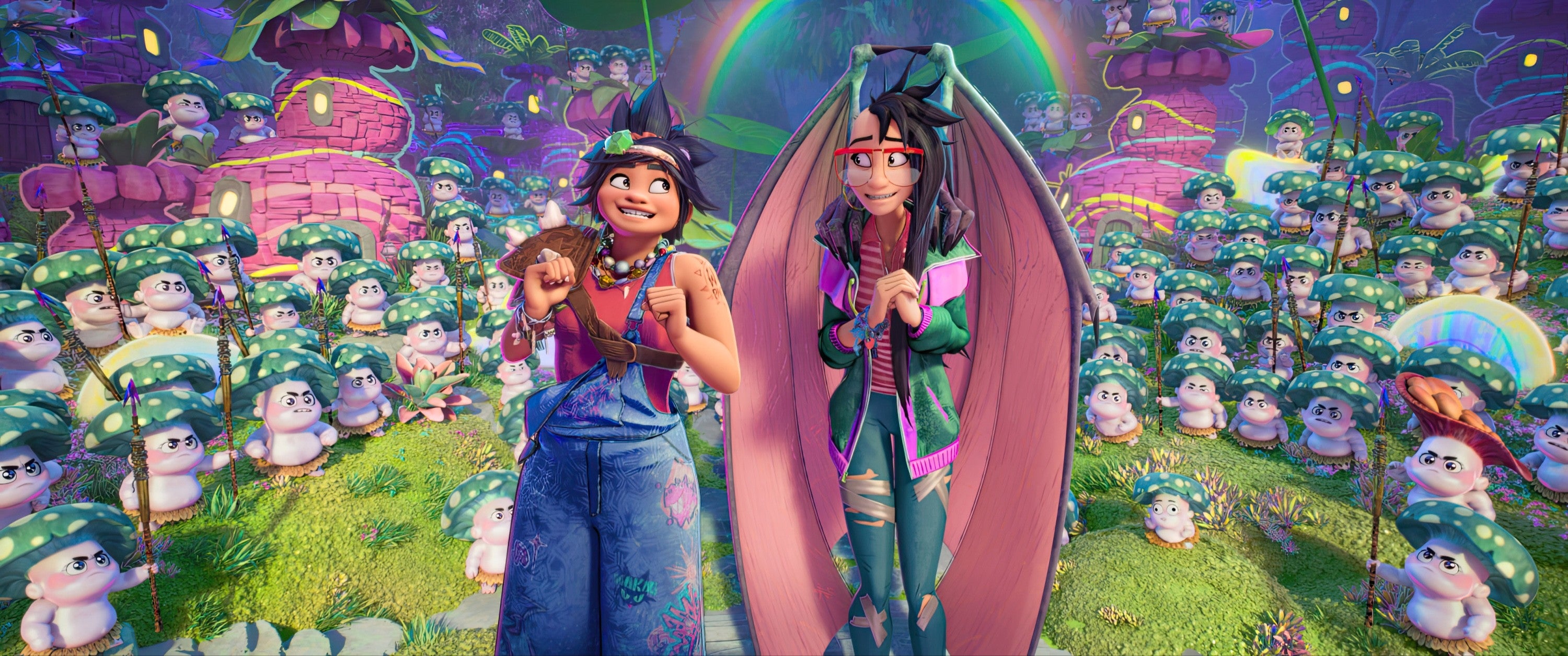 Joe and Raissa smiling in a whimsical, colorful forest filled with mushroom creatures, under a rainbow