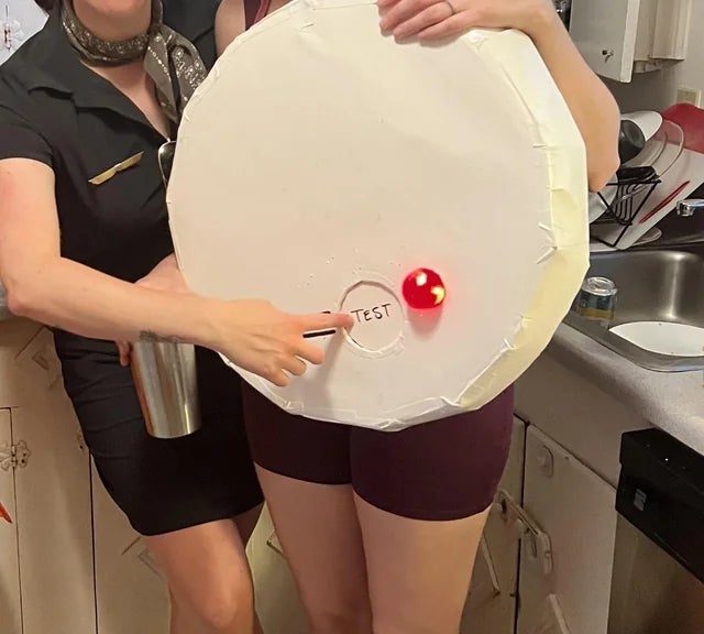 Two radical dressed successful minimalist outfits are holding a mock CD costume that has the connection "TEST" written connected it