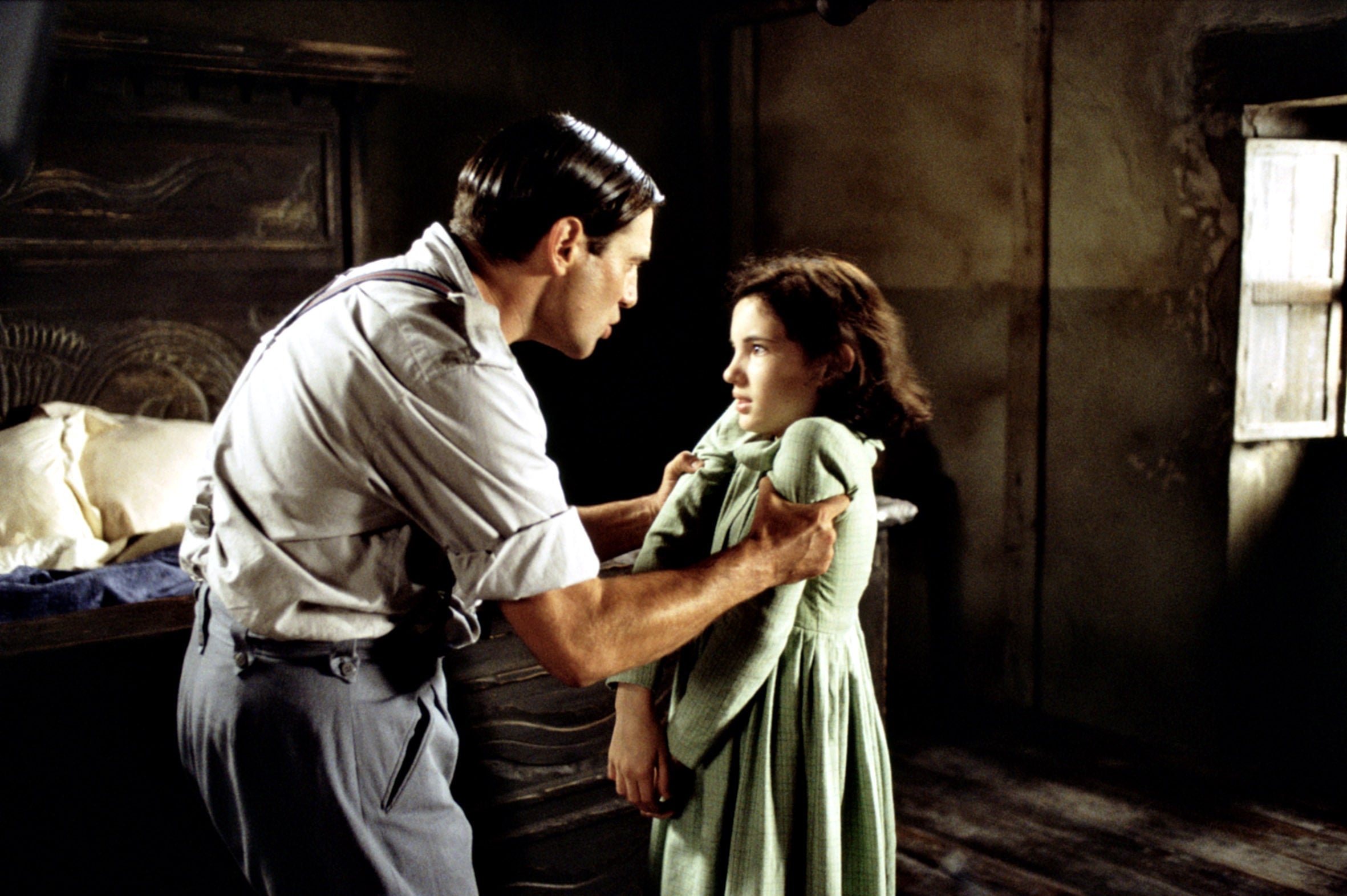 A man in a 1940s-style outfit forcefully holding a young girl by her shoulders in a dimly lit room