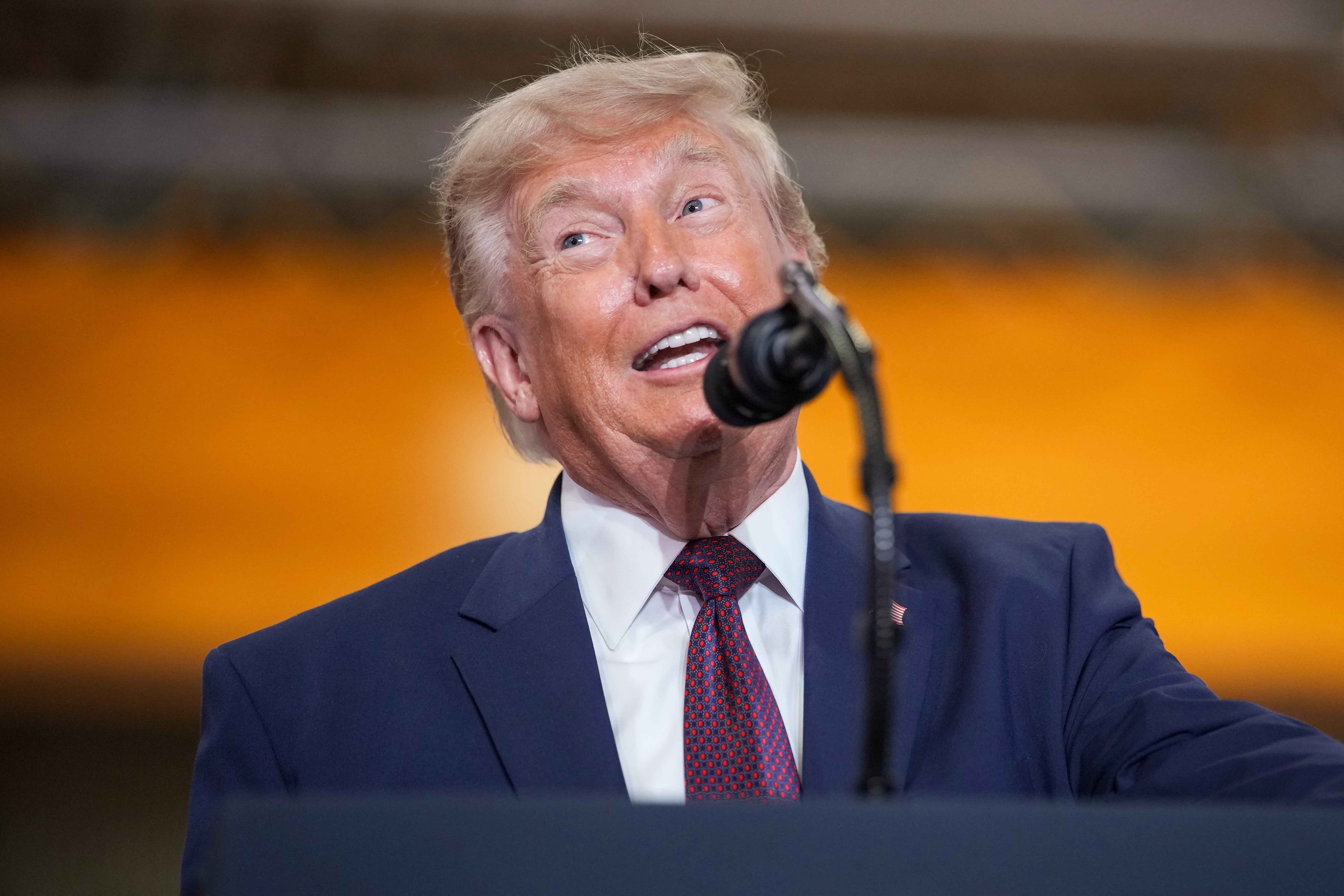 A person in a suit speaks energetically at a podium with a microphone