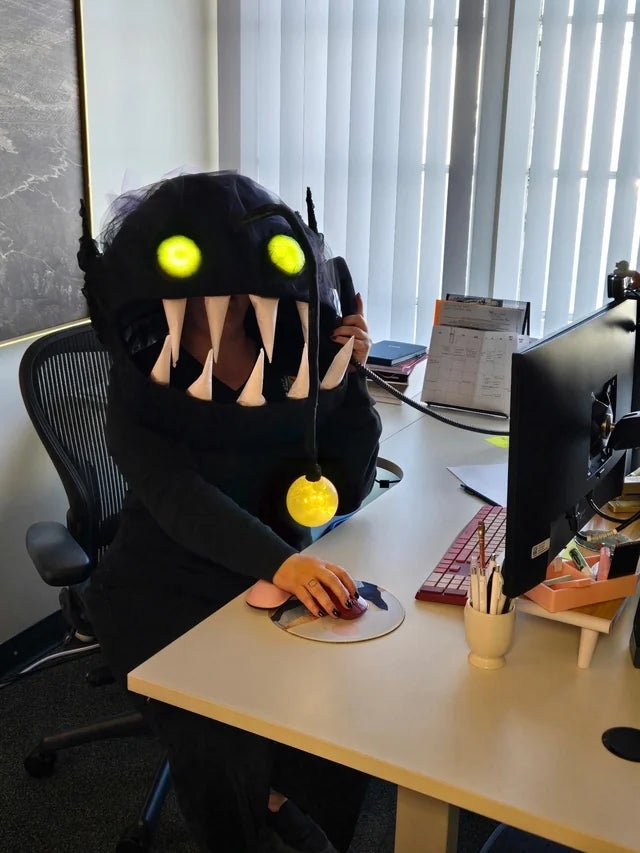 Person astatine a table wearing a deep-sea anglerfish costume with glowing eyes and lure, utilizing a machine mouse