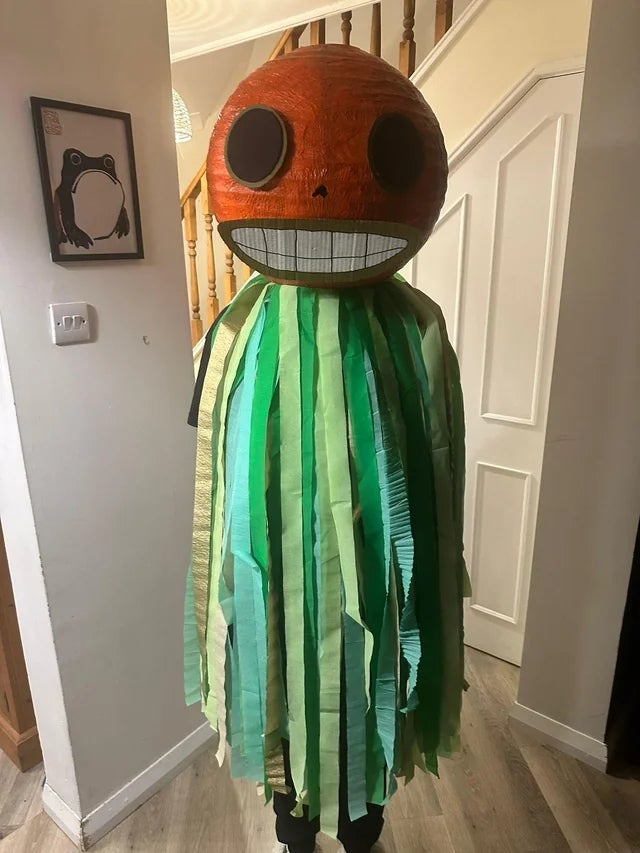 Person successful costume with ample circular caput featuring a wide grin and large eyes, wearing a greenish and yellowish fringed outfit