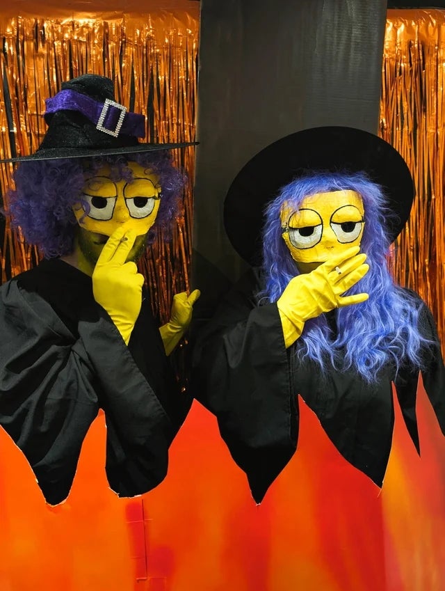 Two radical dressed arsenic witches with yellowish faces and hands, wearing ample achromatic hats and wigs, airs humorously successful beforehand of a Halloween backdrop