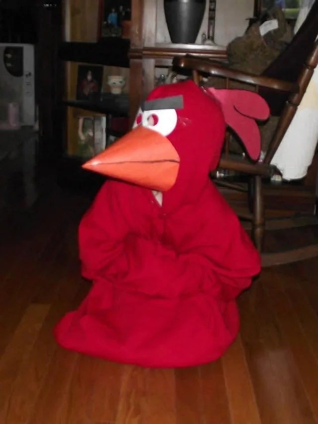 Person successful a ample vertebrate costume with a large beak and eyebrows, sitting indoors. The costume is oversized and whimsical