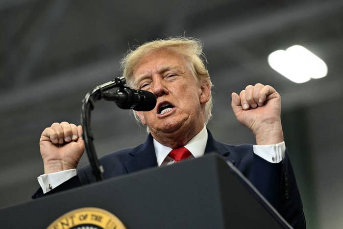 A idiosyncratic   is speaking into a microphone connected  a podium, raising their hands, appearing to beryllium  addressing an assemblage  astatine  an event