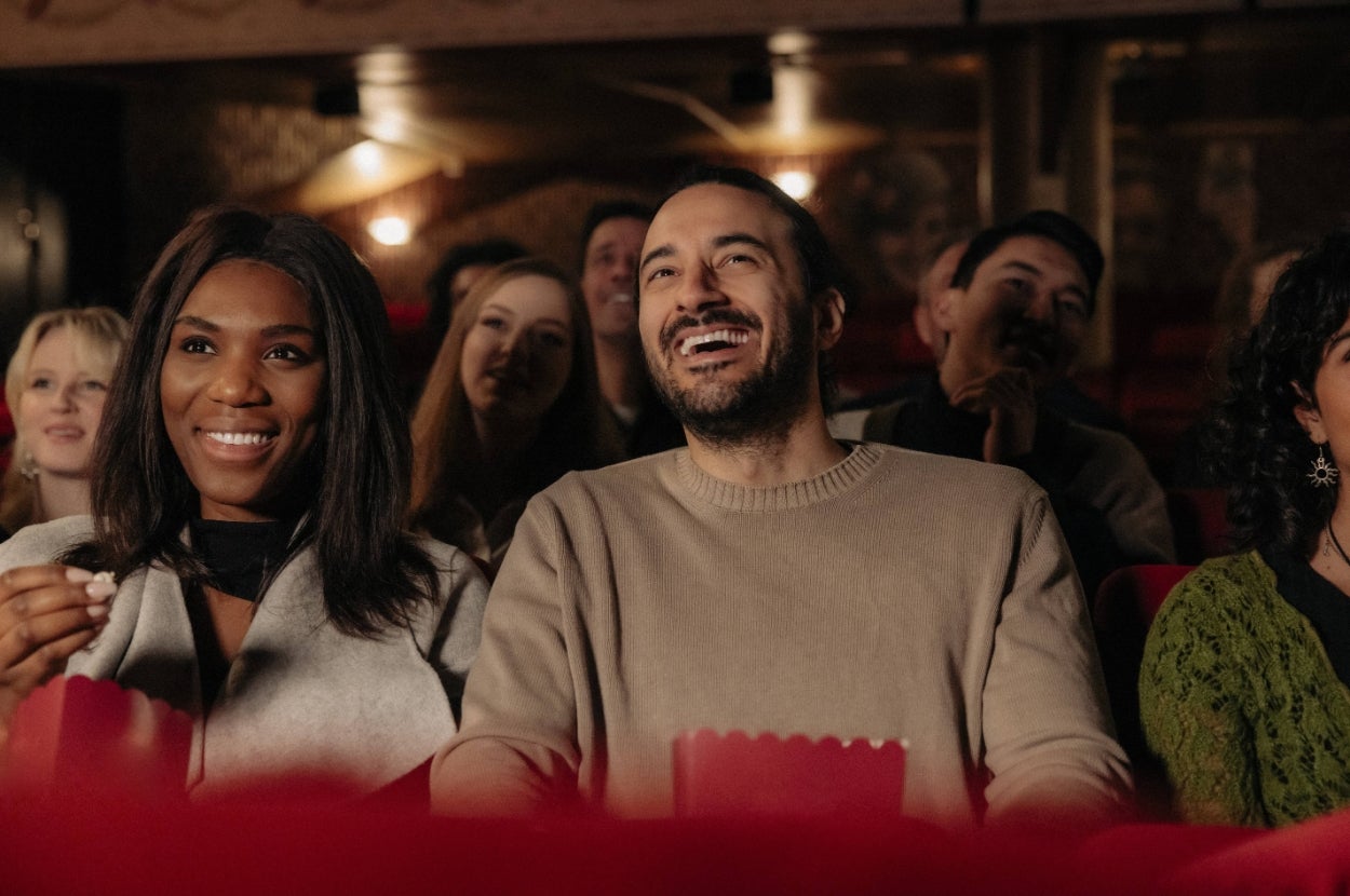 Audience smiling and enjoying a movie in a theater, holding popcorn