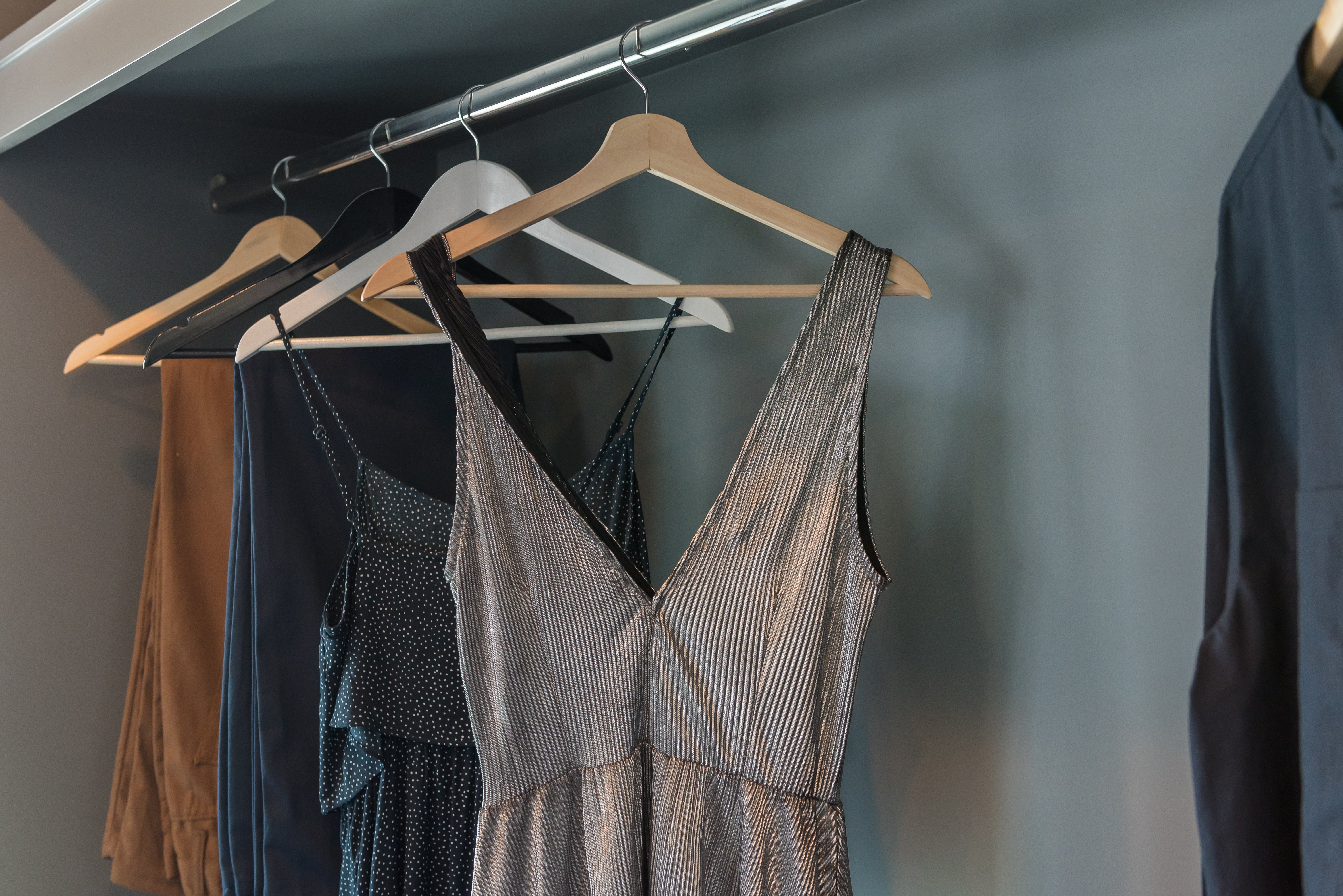 Clothes hanging in a closet, including a sleeveless dress with a V-neck, pants, and shirts on hangers, indicating a neat organization