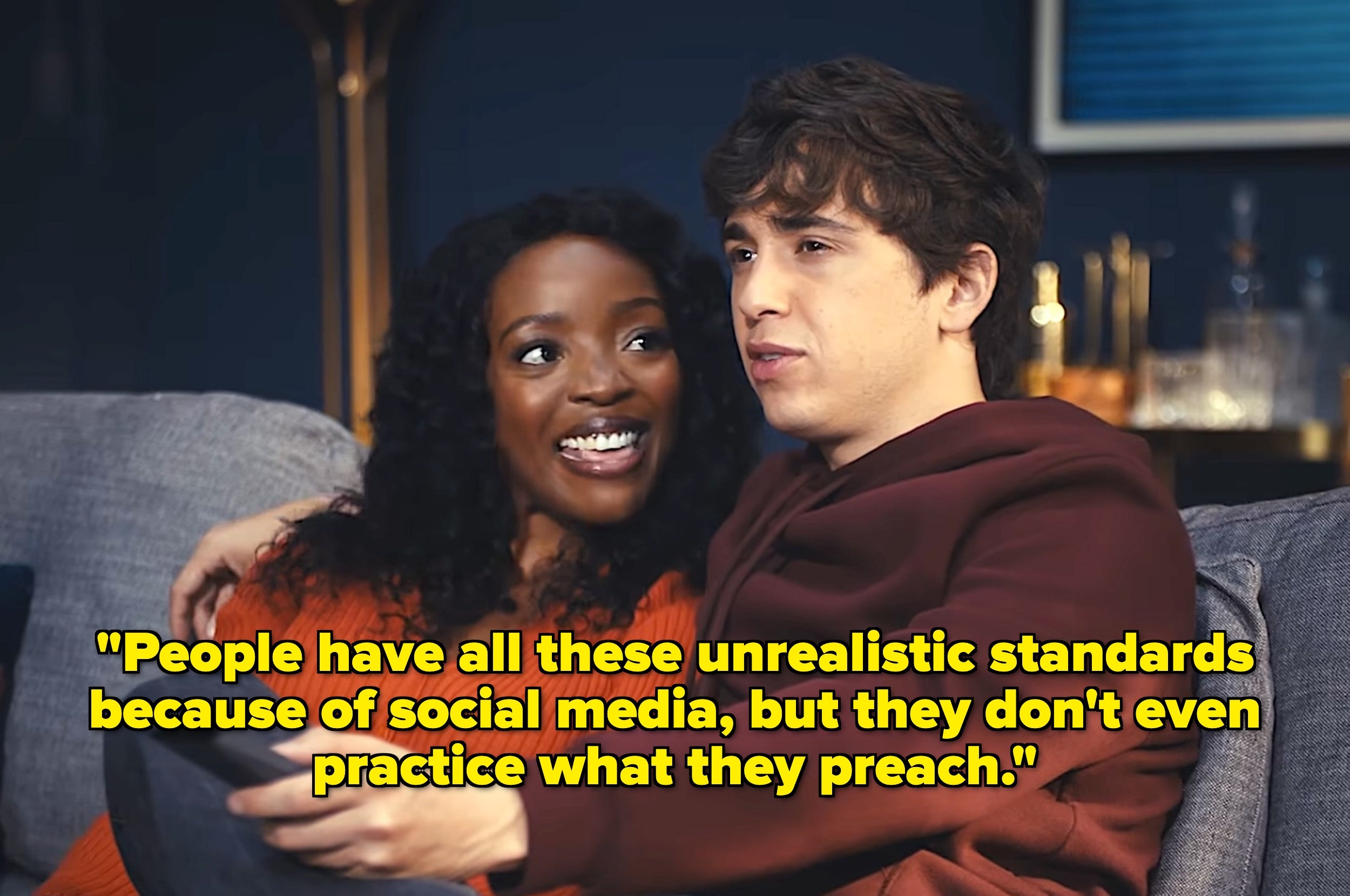 A couple cuddles on a couch, smiling. Text overlaid: "People have unrealistic standards because of social media, but don't practice what they preach."