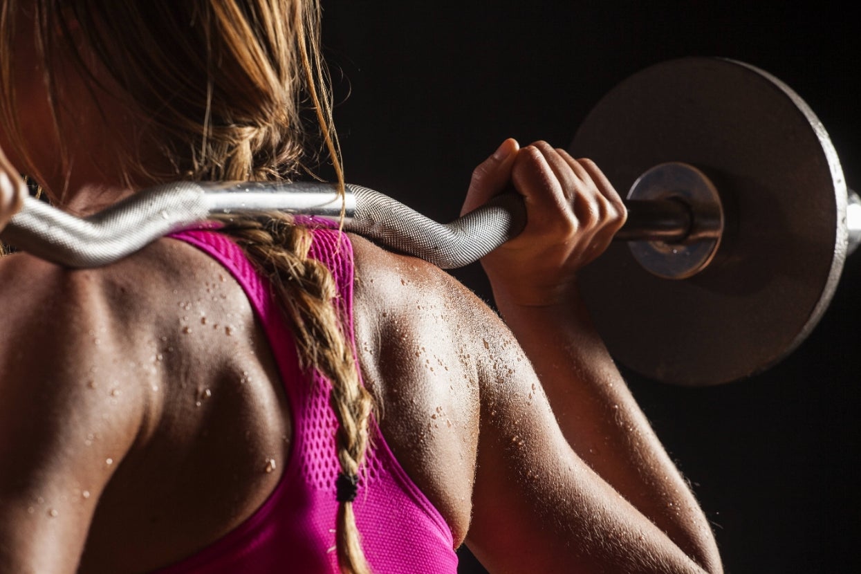 Person lifting a barbell, visible from behind, with sweat glistening on their skin. Their hair is braided