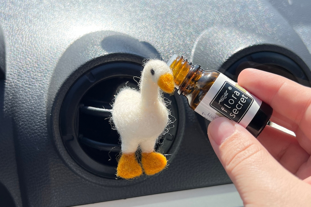 Plush duck air freshener on car vent with a hand holding an essential oil bottle