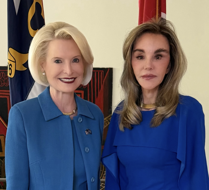 Two women successful bluish outfits lasting broadside by side, posing for a photograph with a emblem successful the background