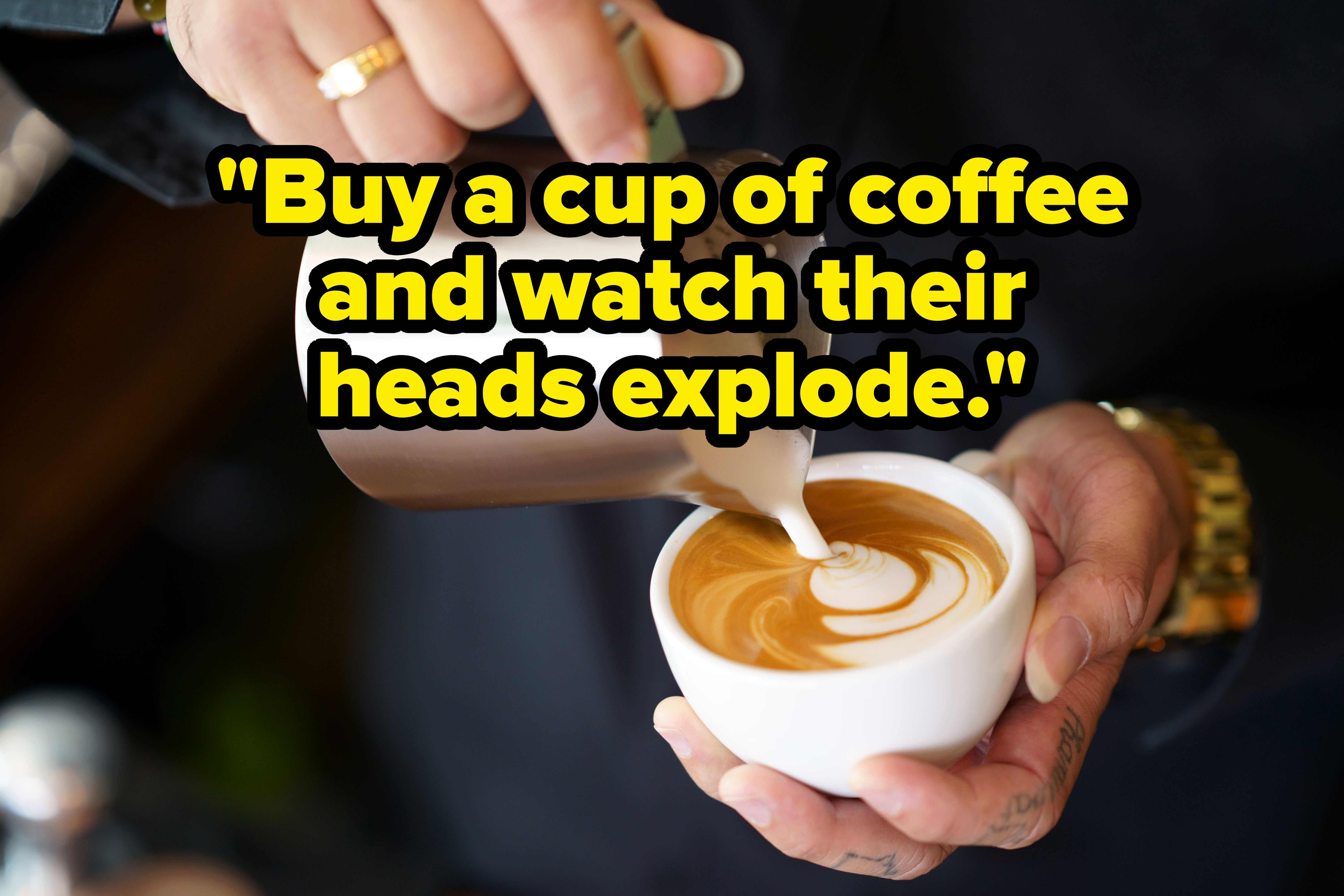 Latte art being poured into a white cup, forming a heart shape. Hands are visible holding the cup and pitcher
