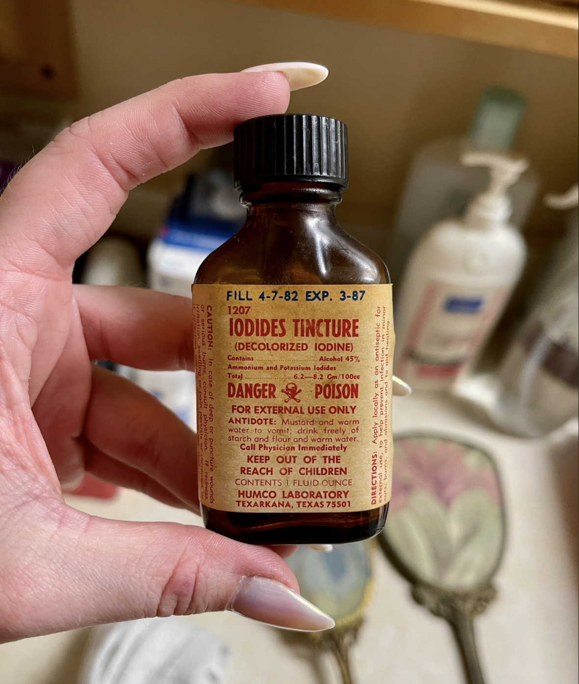 Hand holding a vintage bottle labeled "Iodides Tincture" with warning of poison for external use, expiring March 1987