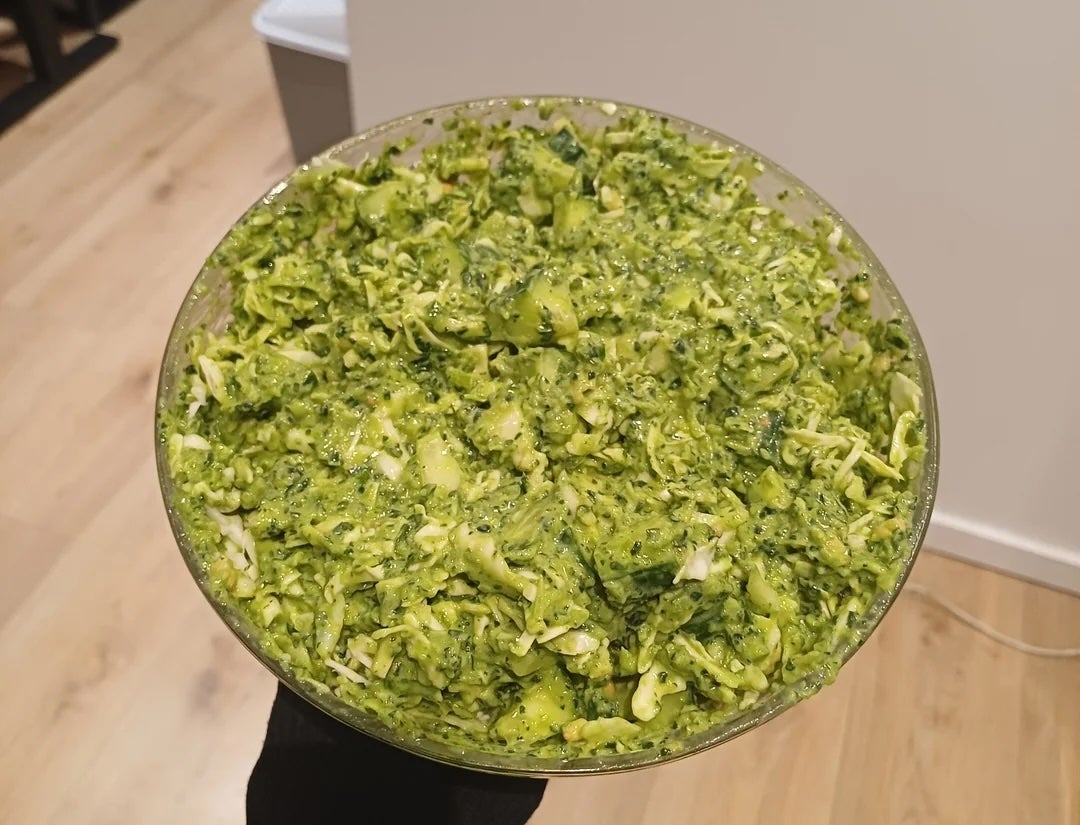 Bowl filled with chopped broccoli salad, mixed with visible herbs and dressing, held against a kitchen background