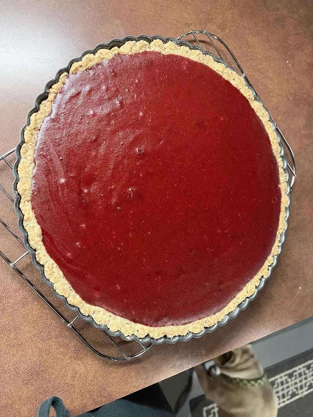 Tart with a glossy, smooth filling in a crumbly crust, cooling on a rack on a kitchen counter