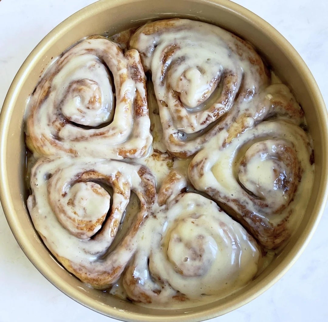 Four freshly baked cinnamon rolls with glaze in a round baking pan
