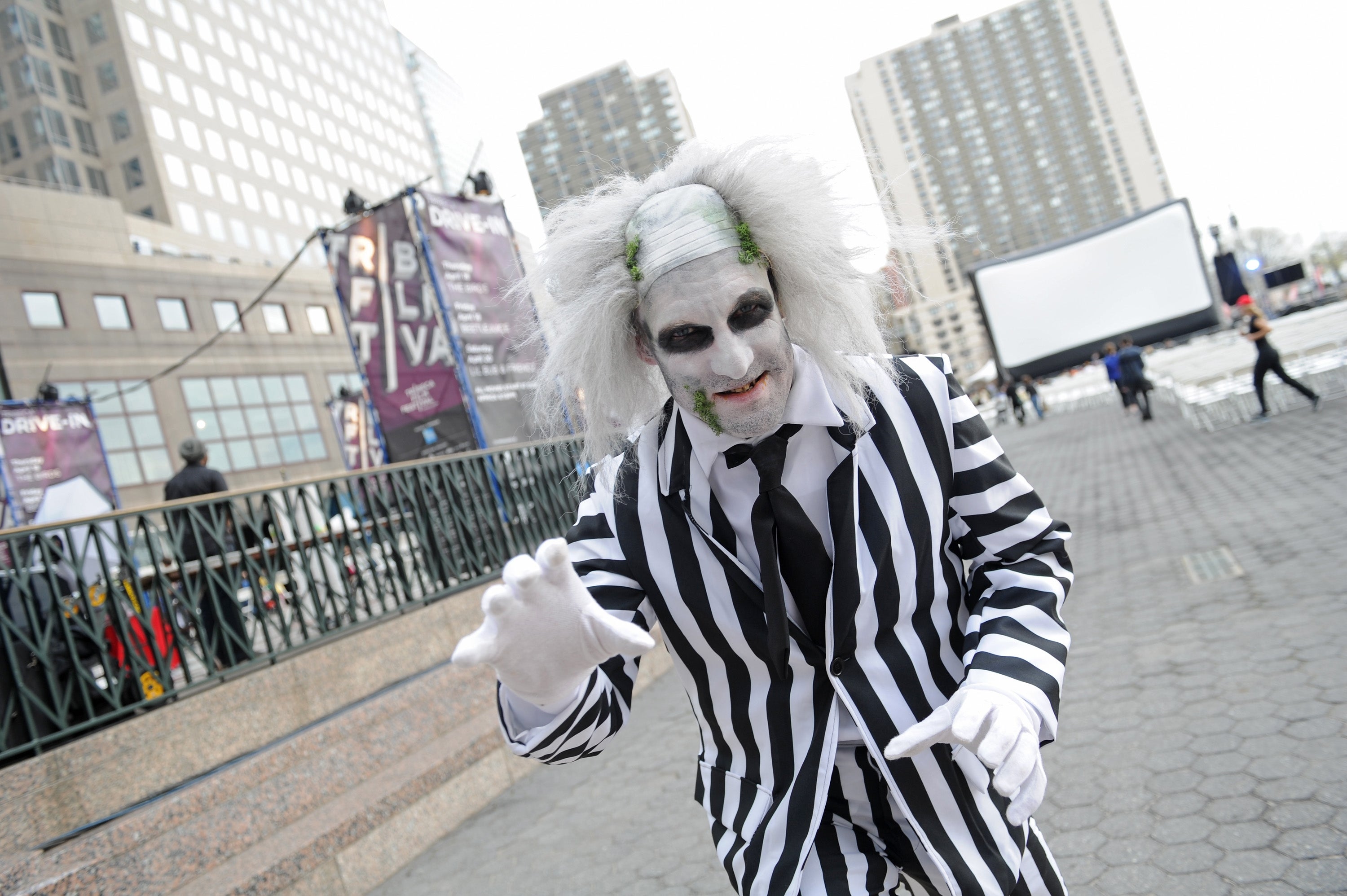 Person successful achromatic and achromatic striped suit and gothic-style makeup, posing playfully outdoors, with buildings successful the background