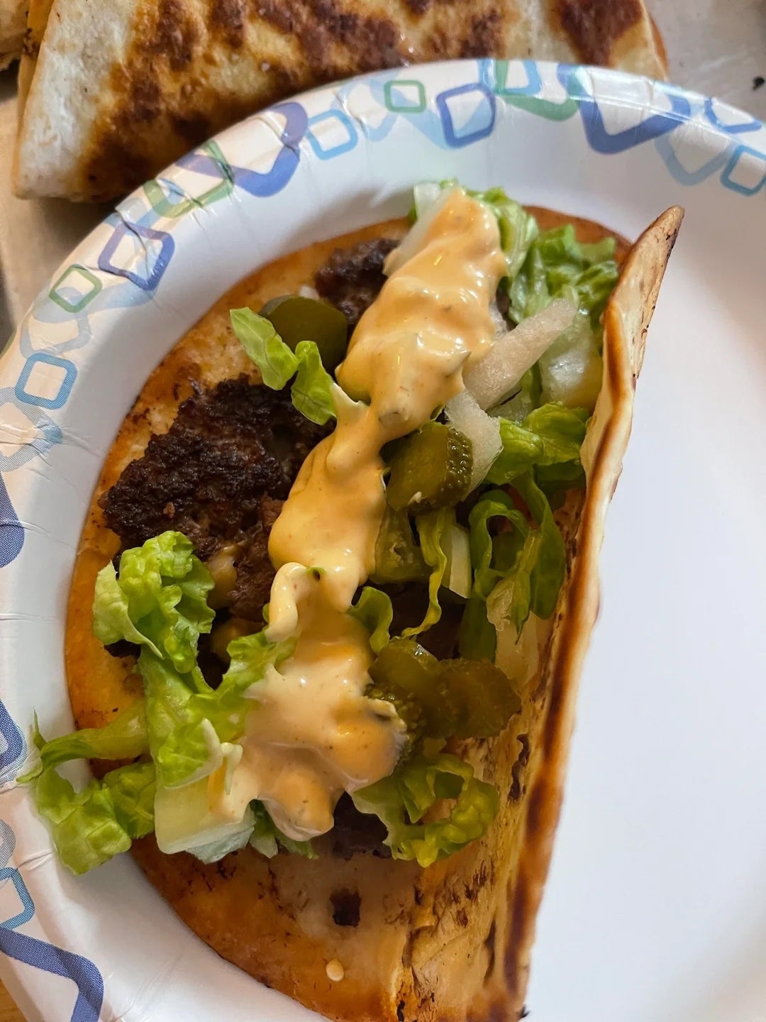 Taco with ground meat, lettuce, pickles, onions, and sauce on a paper plate