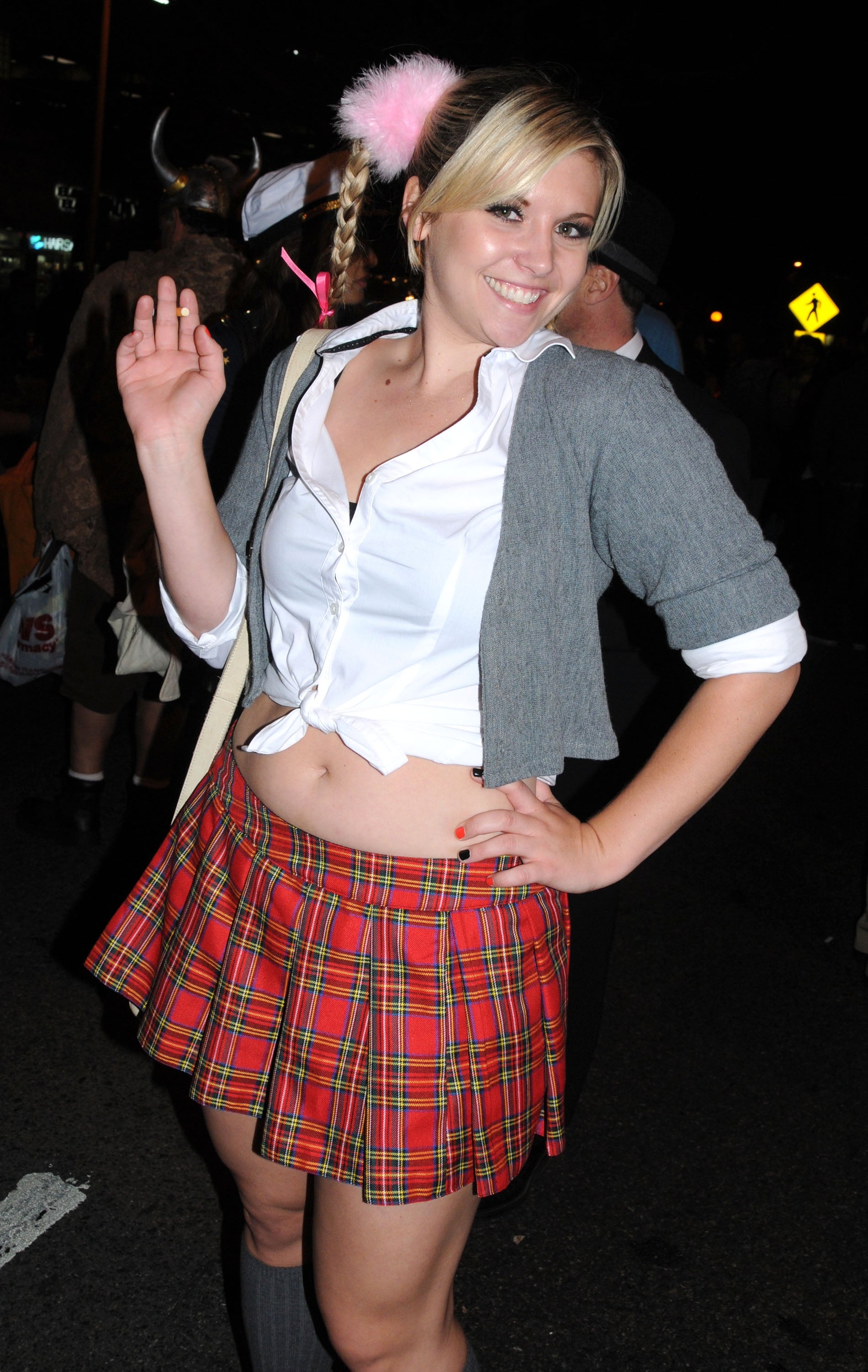 Person successful a schoolgirl-inspired outfit with a plaid skirt, grey cardigan, and achromatic garment astatine a nationalist event, smiling and waving astatine the camera