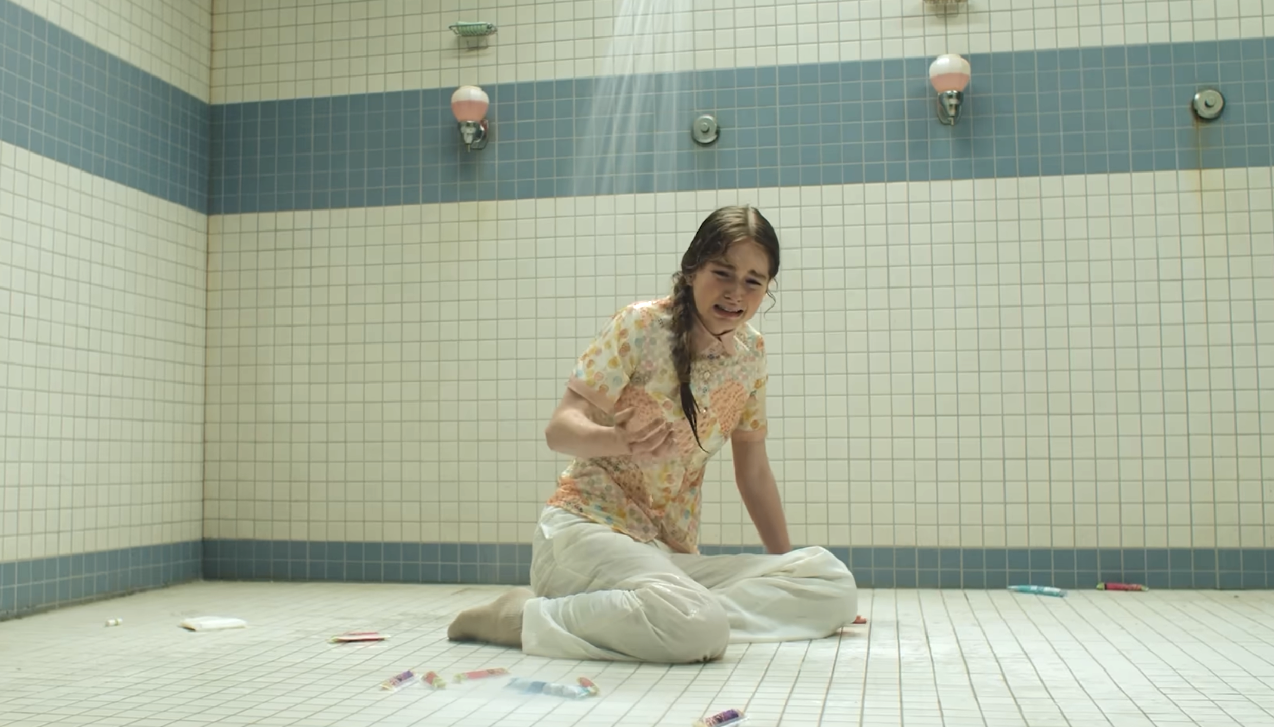 Carrie sits on a tiled floor in a bathroom, surrounded by scattered markers,