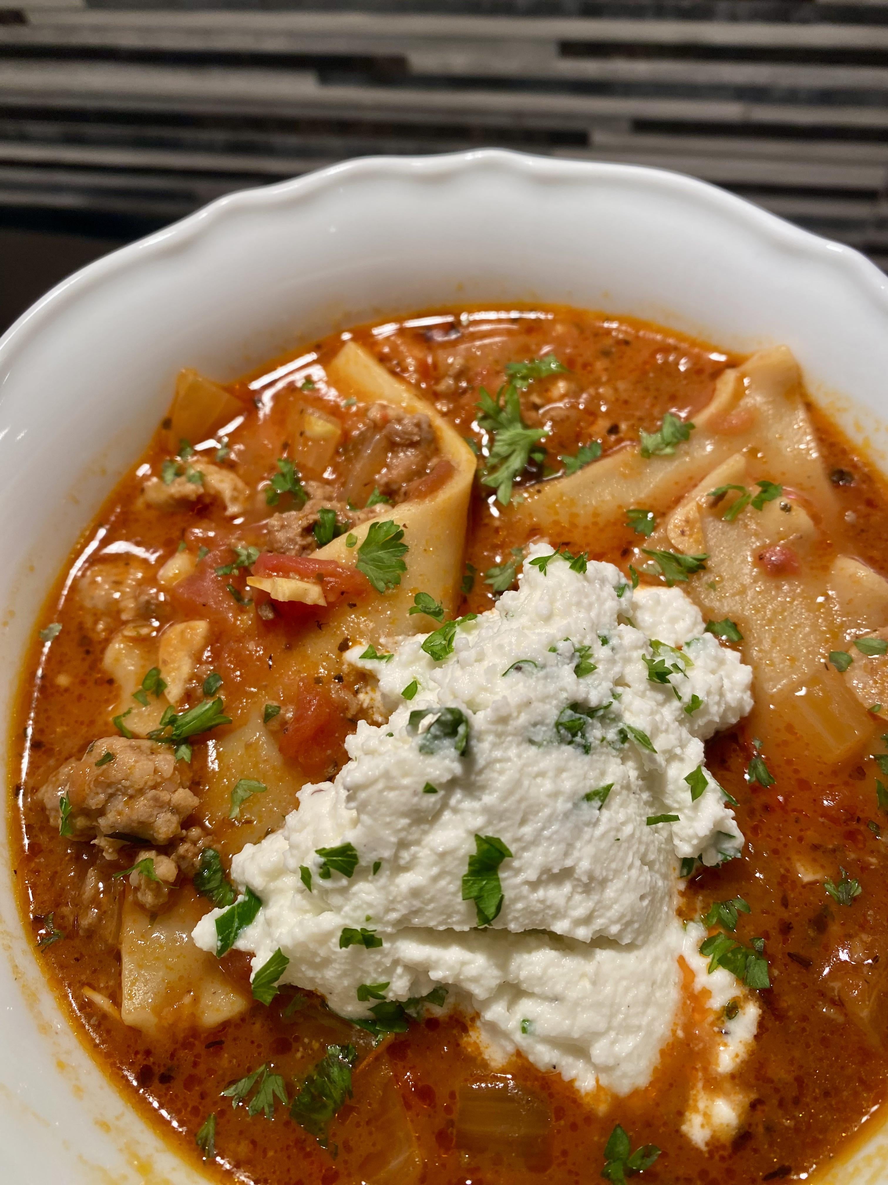 A bowl of lasagna soup with ricotta cheese and parsley garnish