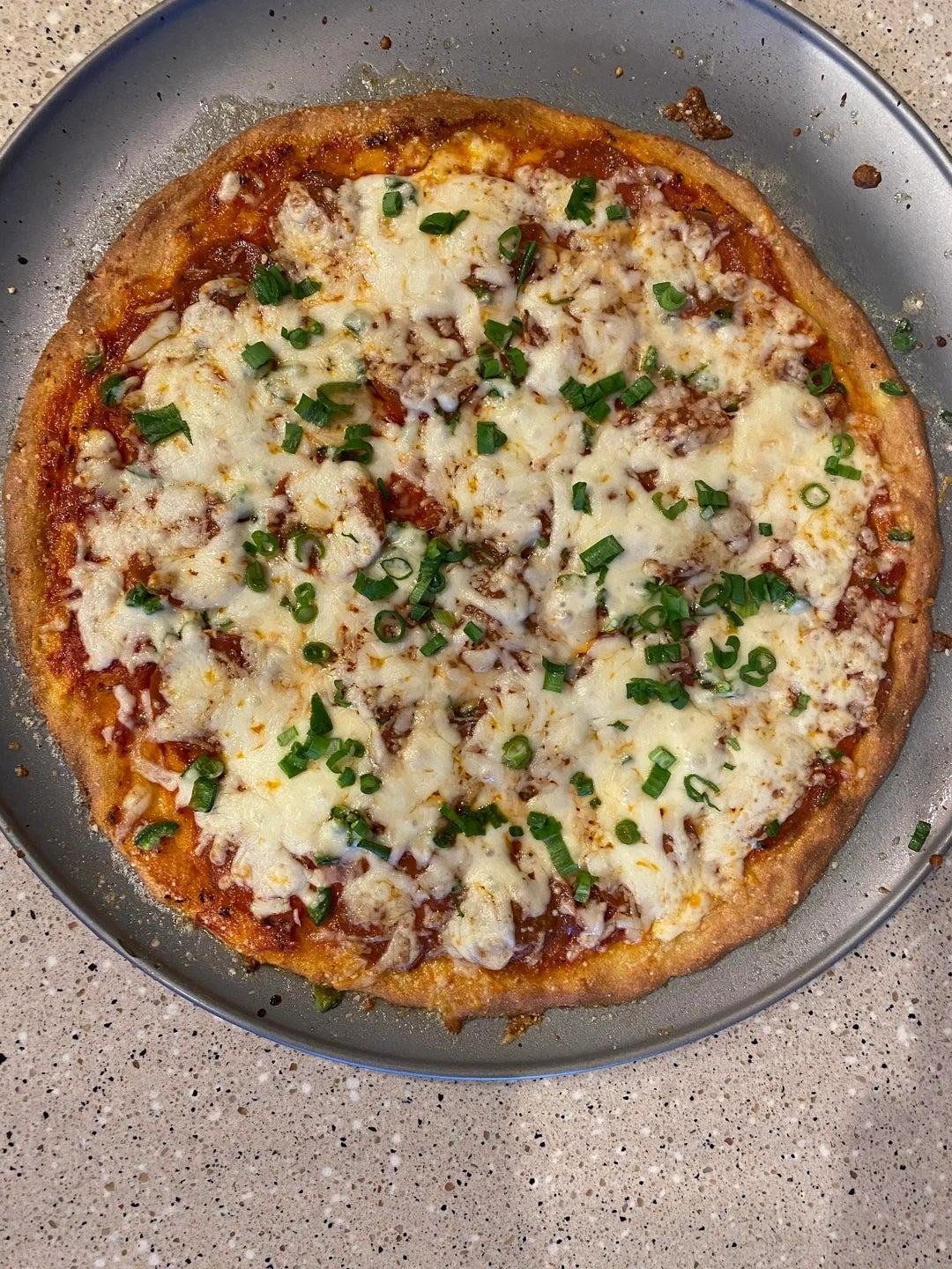 A freshly baked pizza topped with melted cheese and chopped green onions on a round metal pan