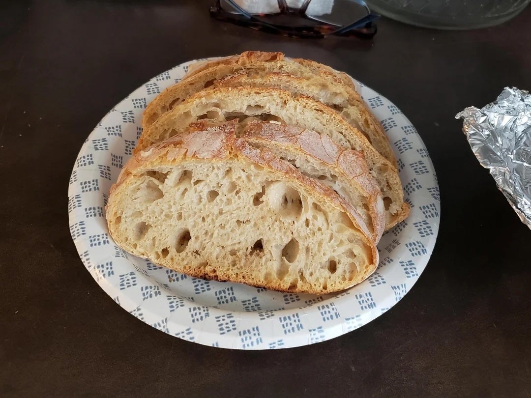 Slices of artisanal bread on a patterned plate, next to crumpled foil and a pair of glasses