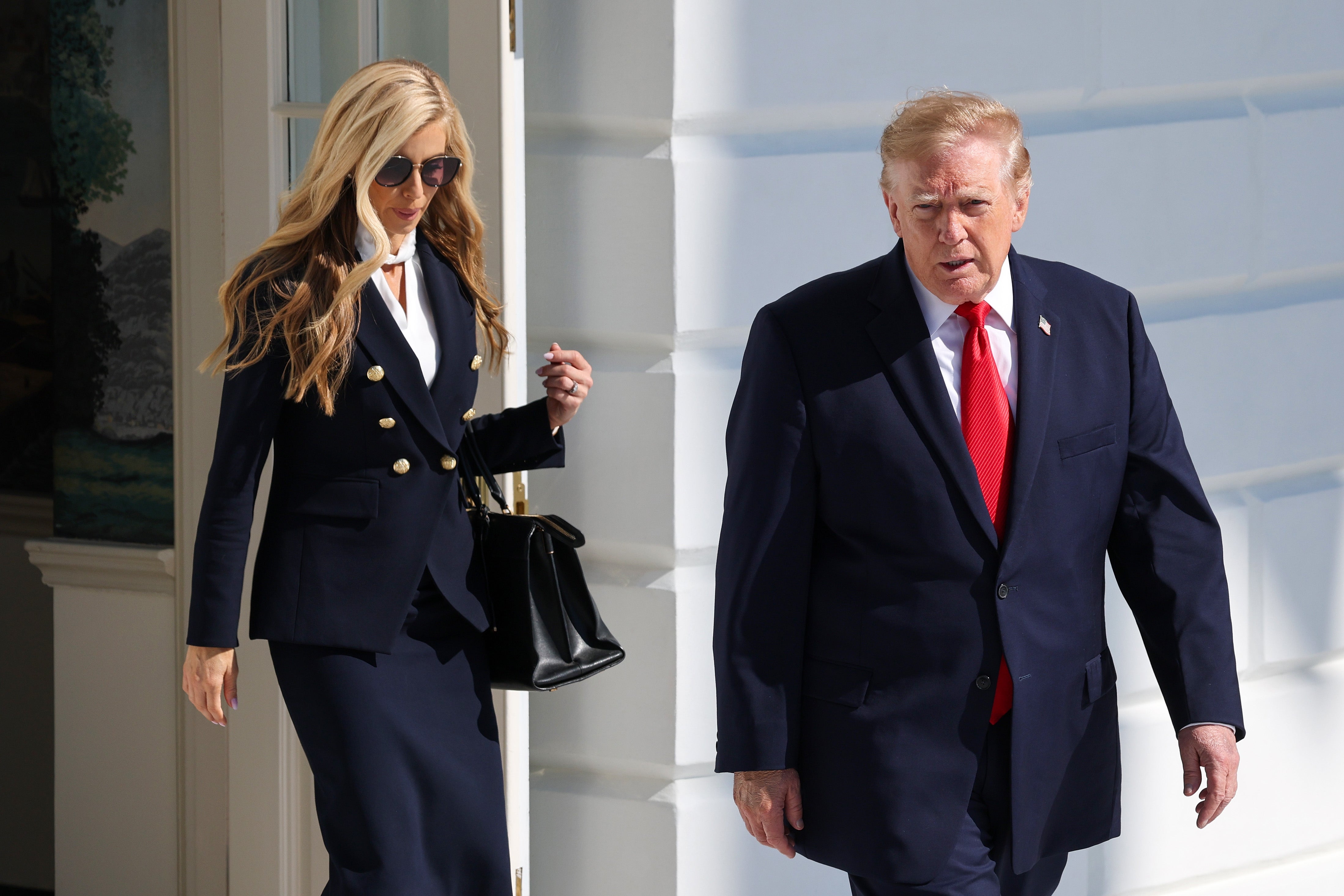 Two individuals successful  ceremonial  attire walking extracurricular  a achromatic  building; 1  wears a double-breasted blazer, the different   a suit   with a reddish  tie