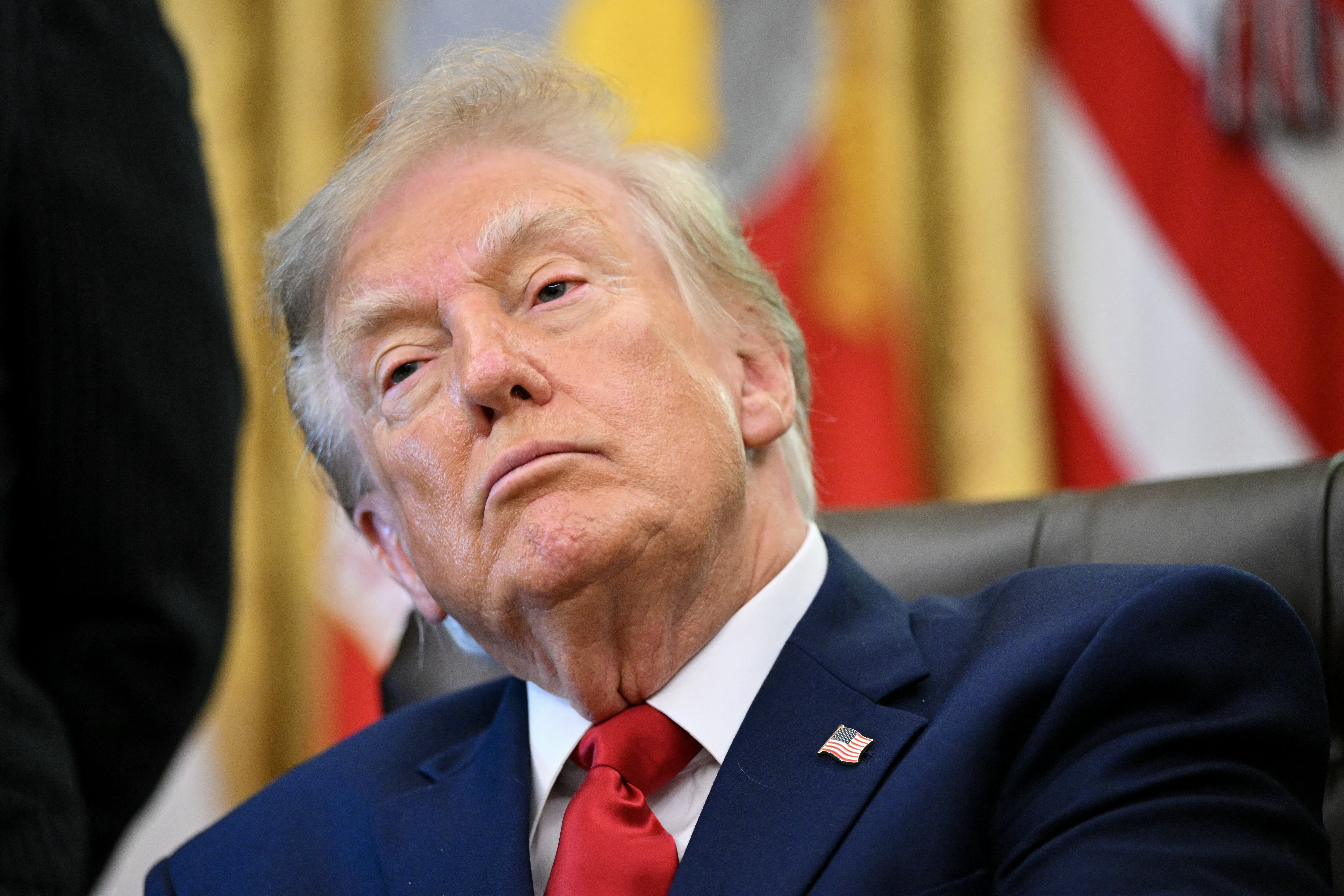 A idiosyncratic   seated astatine  a desk, wearing a suit   and looking contemplative, with flags disposable   successful  the background