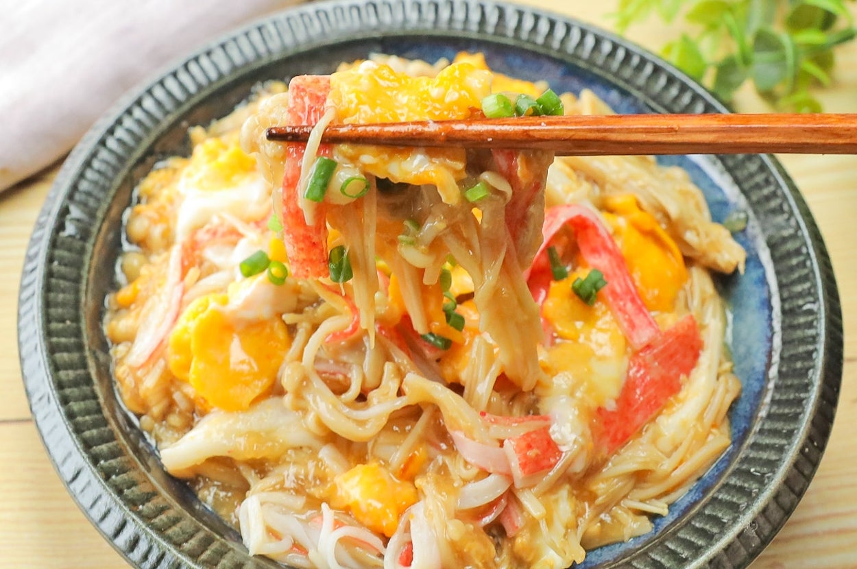蟹カマと卵が乗った和風丼。箸でひと口取られています。背景に植物。