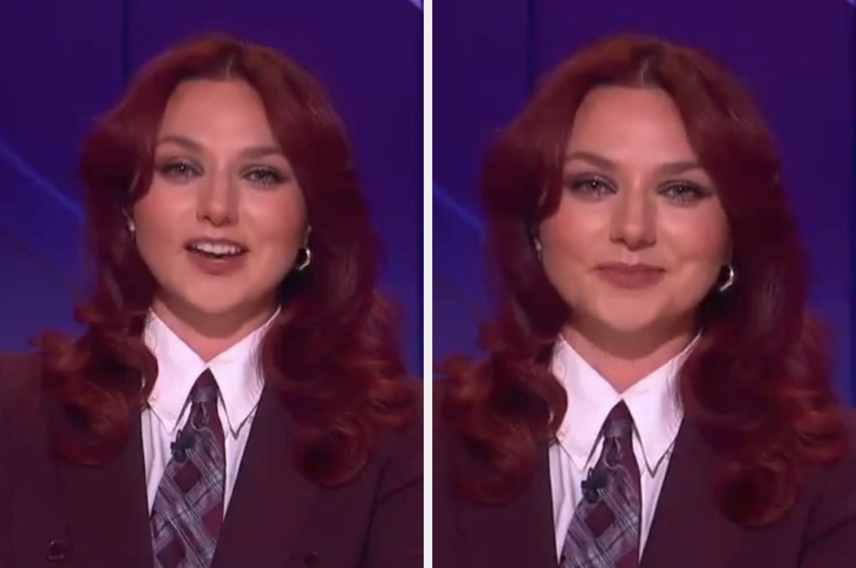 A person with long hair and a plaid tie speaks on camera, wearing a formal shirt and blazer