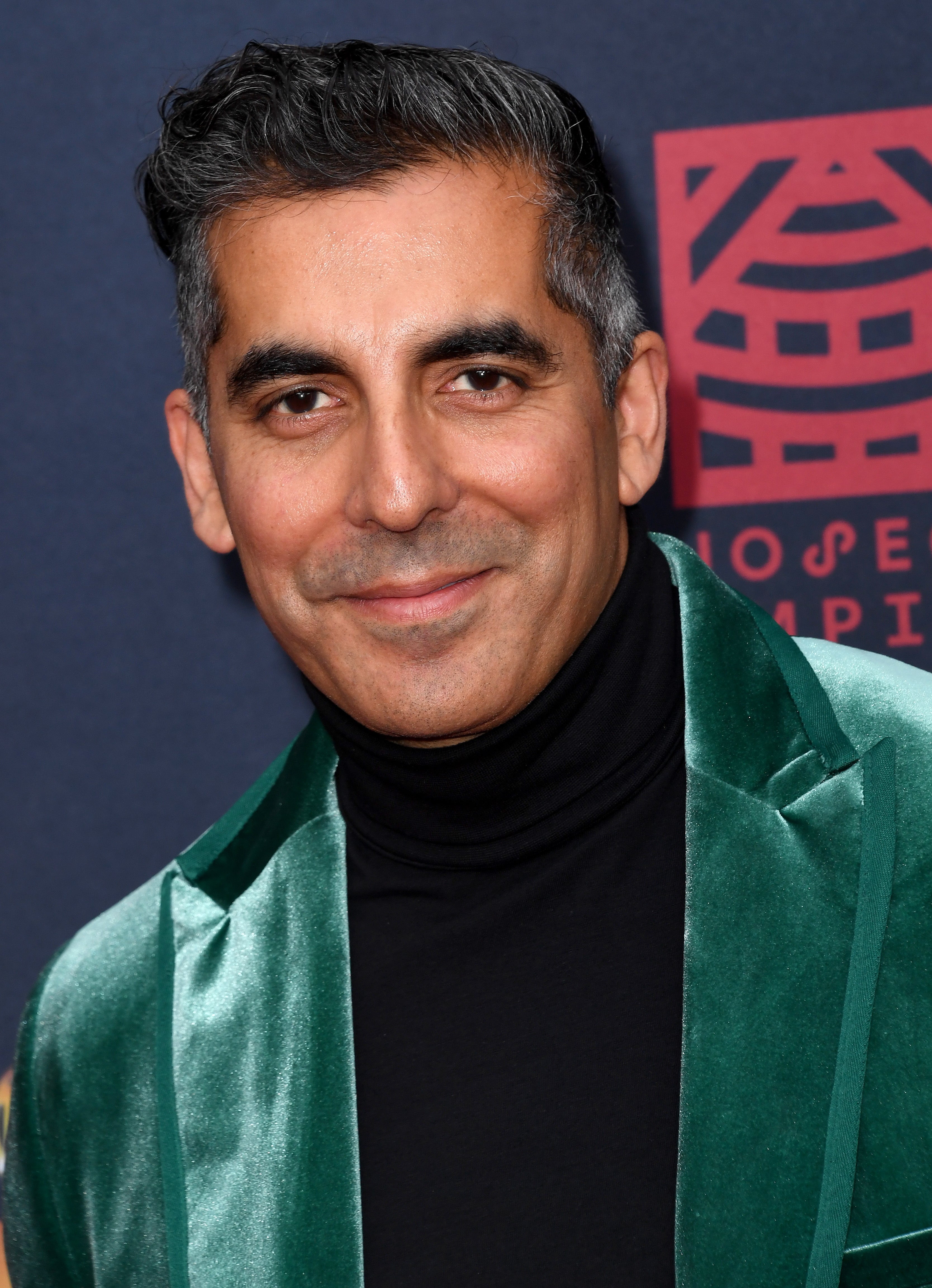 Actor Sunil Malhotra, wearing a velvet overgarment and turtleneck, poses with a flimsy smile, lasting against a acheronian backdrop.