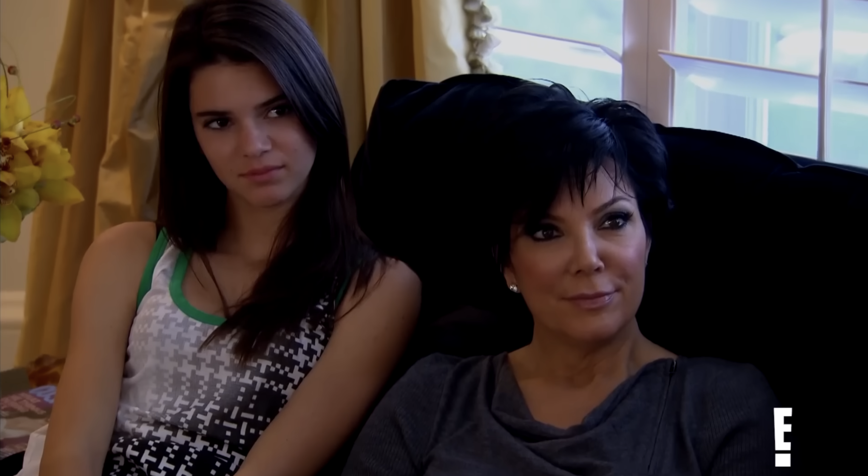 Kendall and Kris seated on a sofa, watching intently. One wears a patterned tank top, the other a simple top. They appear focused and engaged