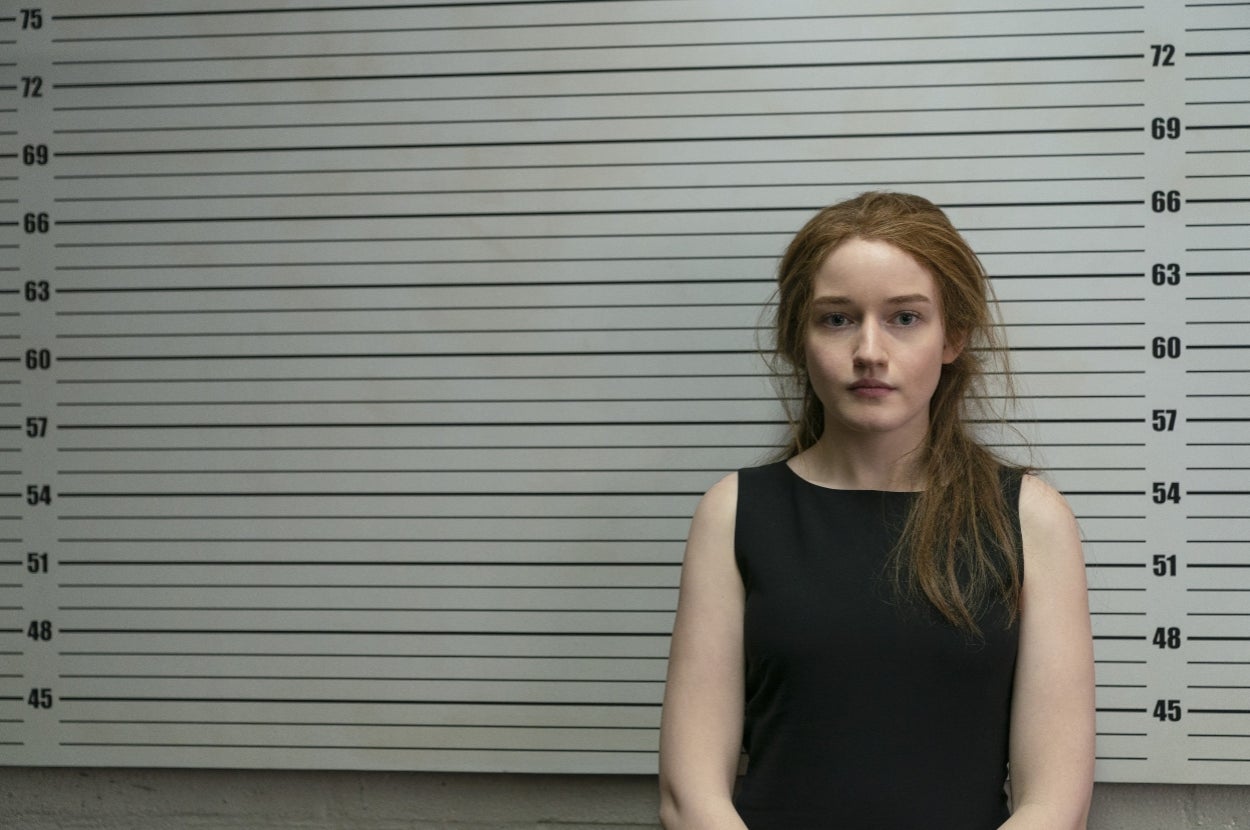 A person stands in front of a height chart in a police mugshot setting, wearing a simple, sleeveless dress