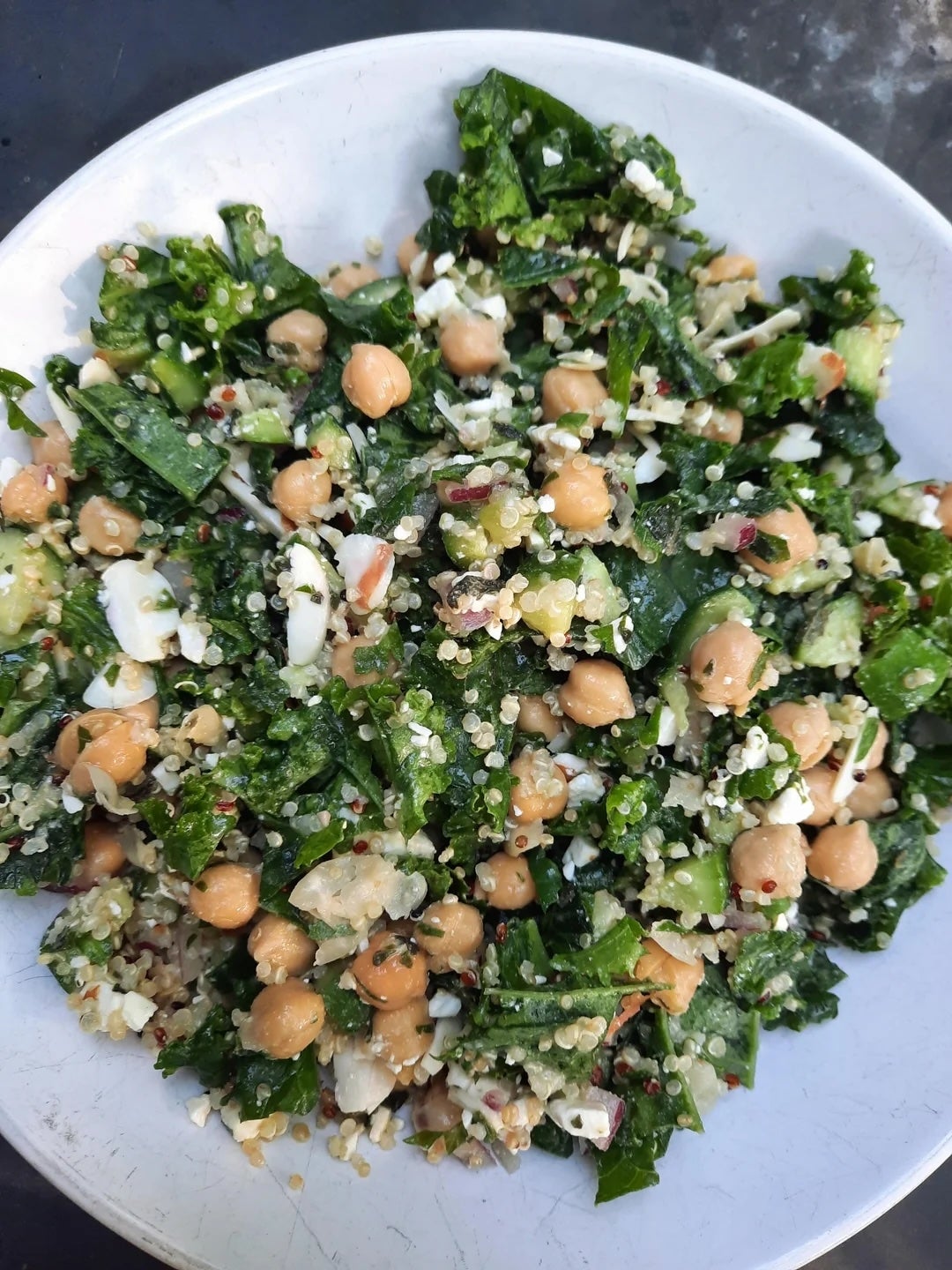 A bowl of salad with kale, chickpeas, quinoa, cucumber, and feta cheese, mixing fresh greens and grains