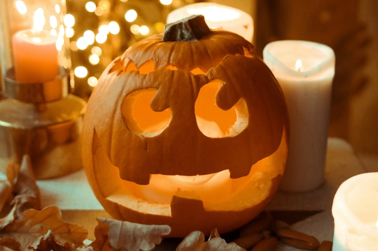 A carved jack-o'-lantern with a smiling face sits among lit candles and autumn leaves