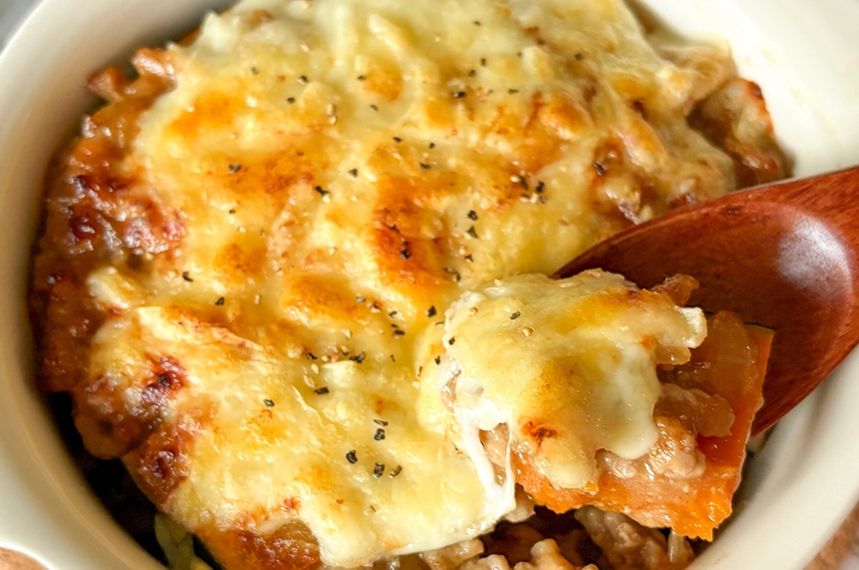 かぼちゃの肉みそチーズ焼きがグラタン皿に盛られ、スプーンですくわれている。とろけたチーズがのっている。