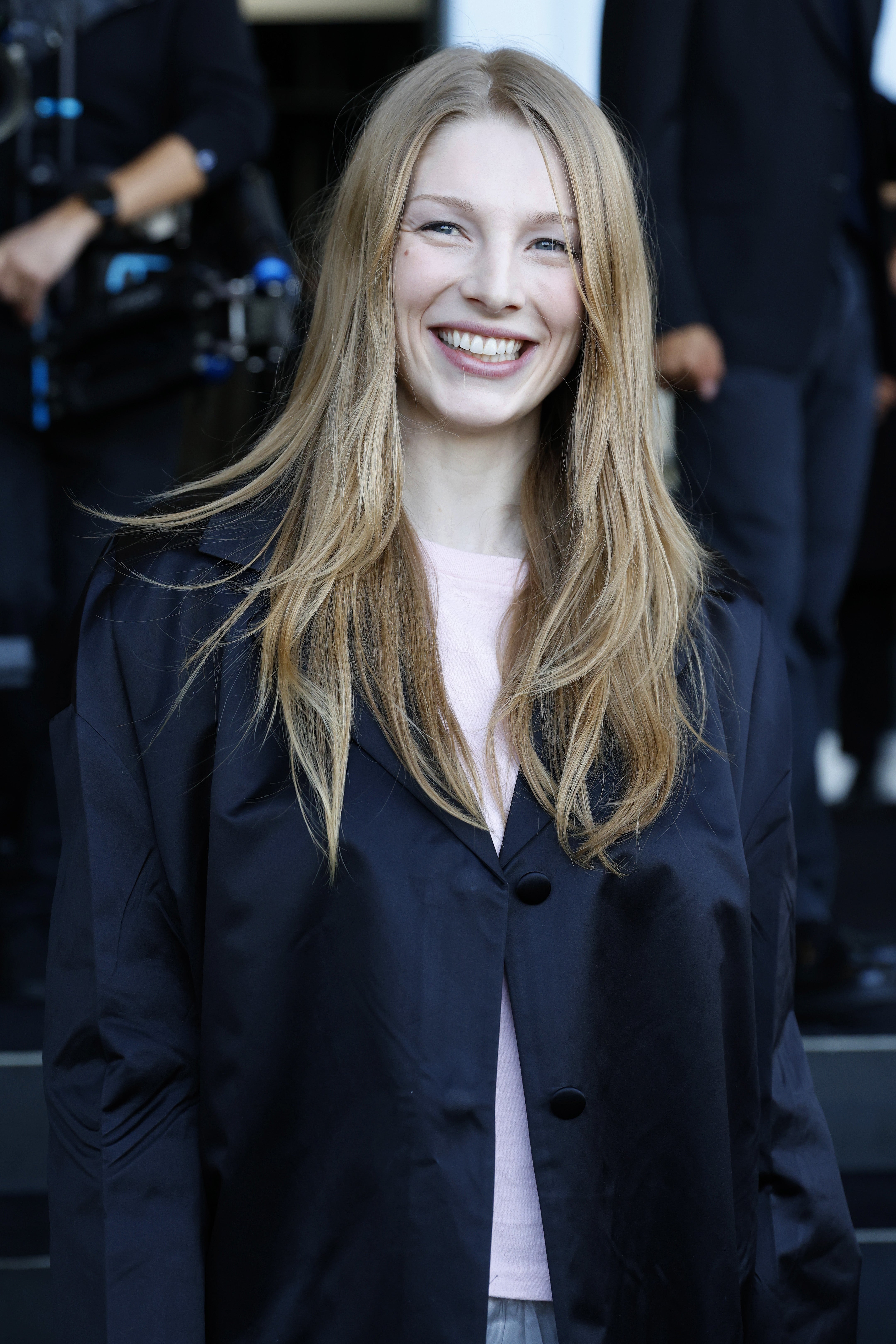A person in a stylish, oversized jacket smiles at a public event