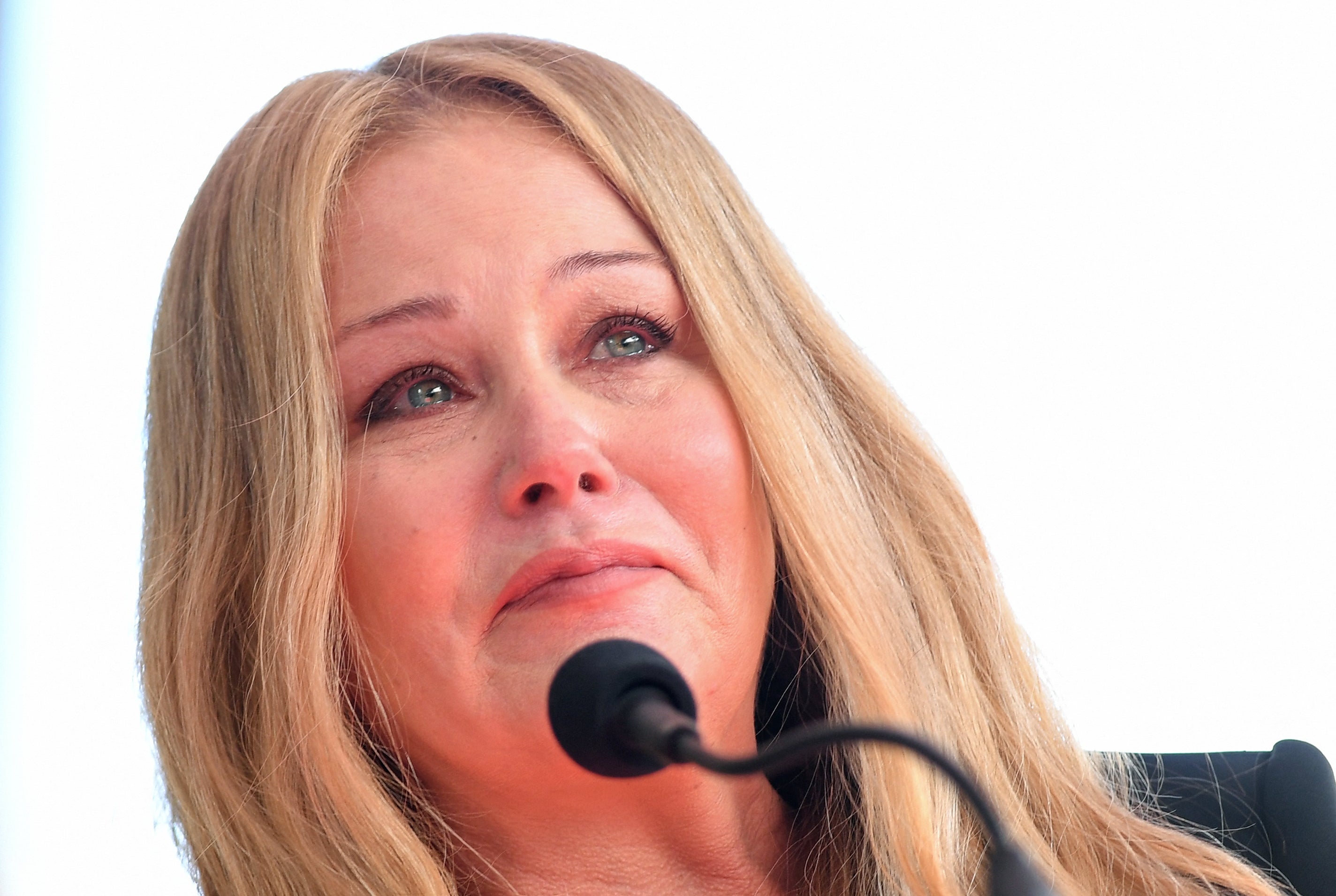 A person with long hair is speaking into a microphone, appearing emotional with tears in their eyes