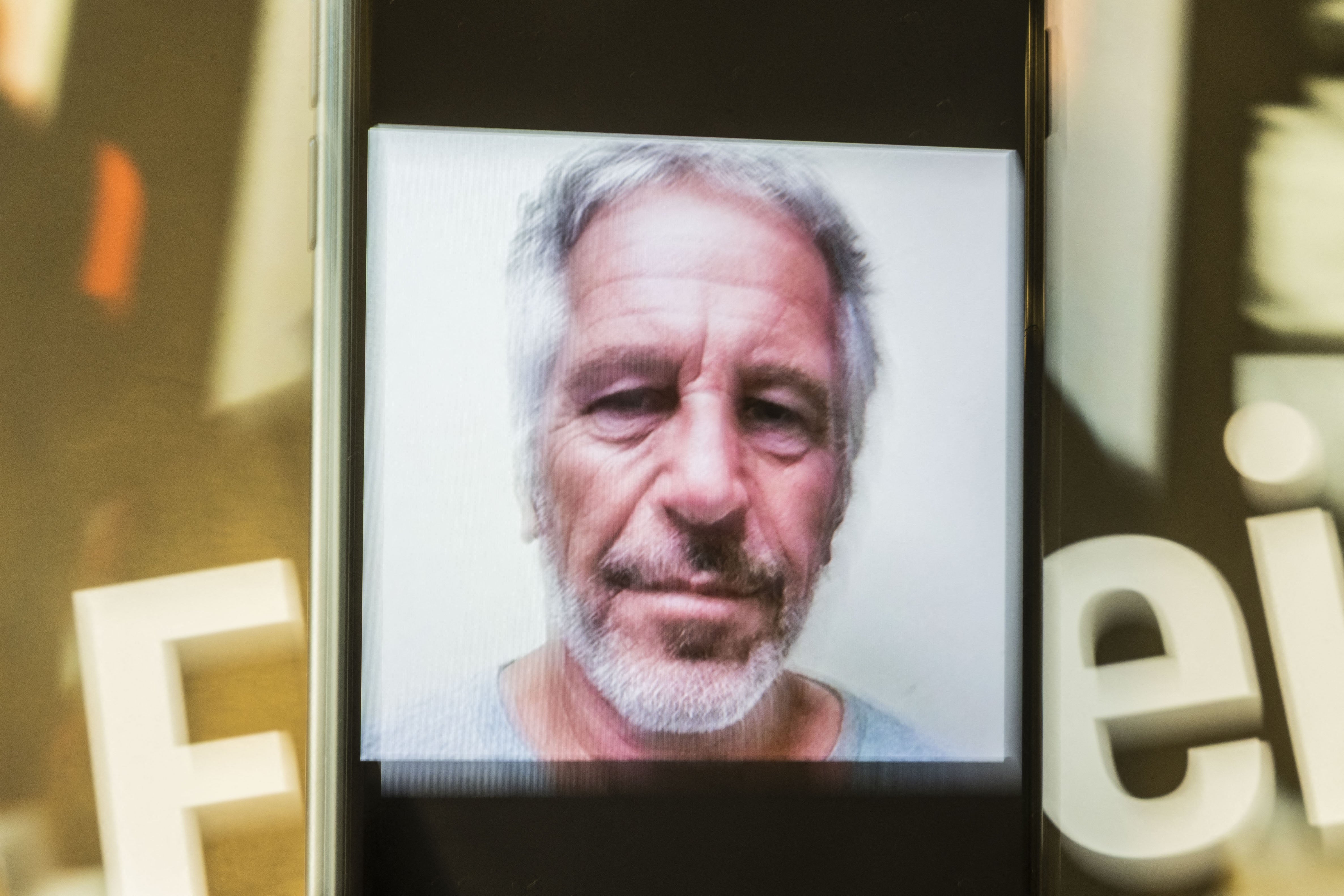 A photograph of Jeffrey Epstein displayed on a smartphone in front of the cover of Aujourd hui en France presenting an investigation into the Epstein case