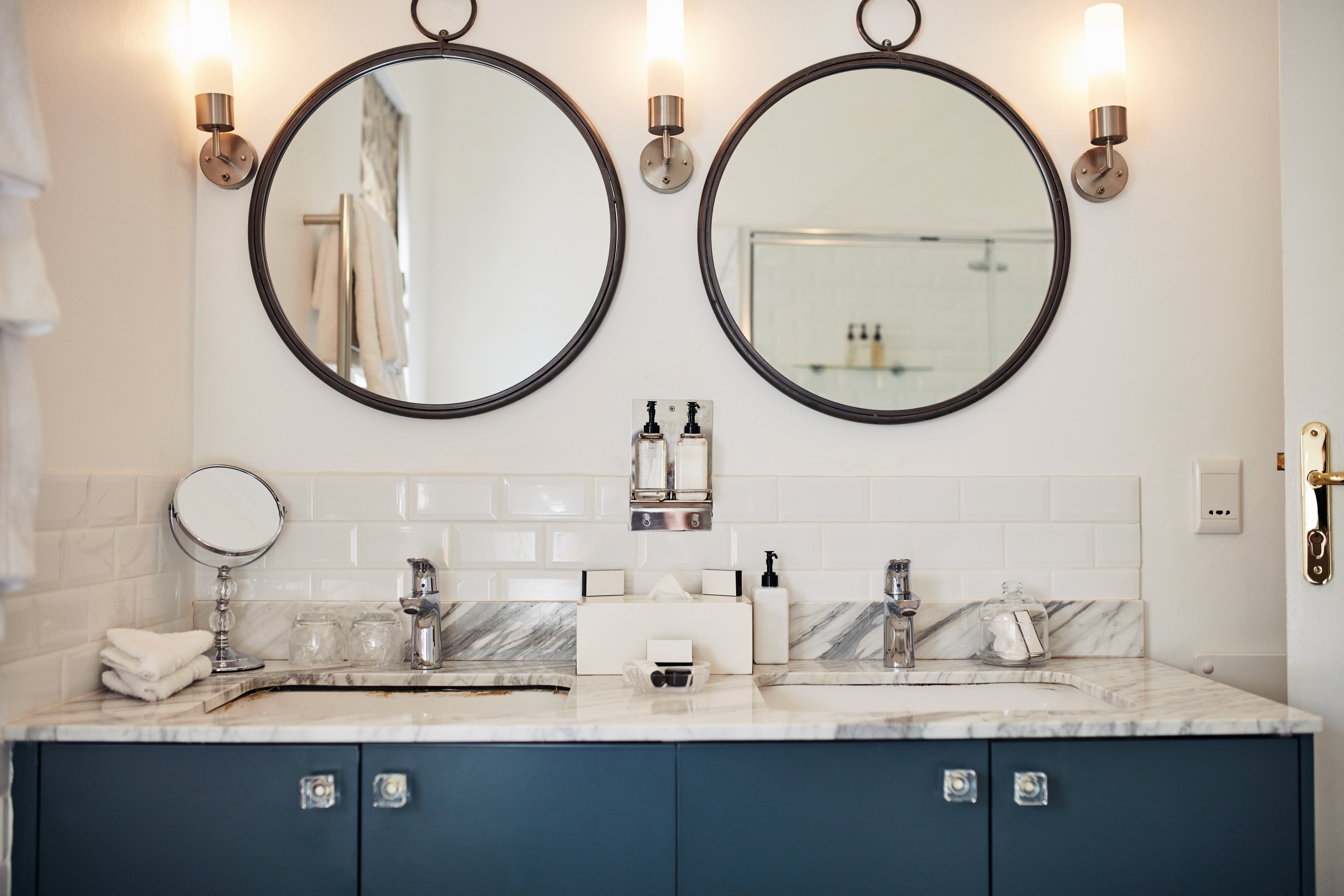 Modern bathroom vanity with dual sinks, round mirrors, and marble countertop, featuring minimalistic decor and elegant lighting