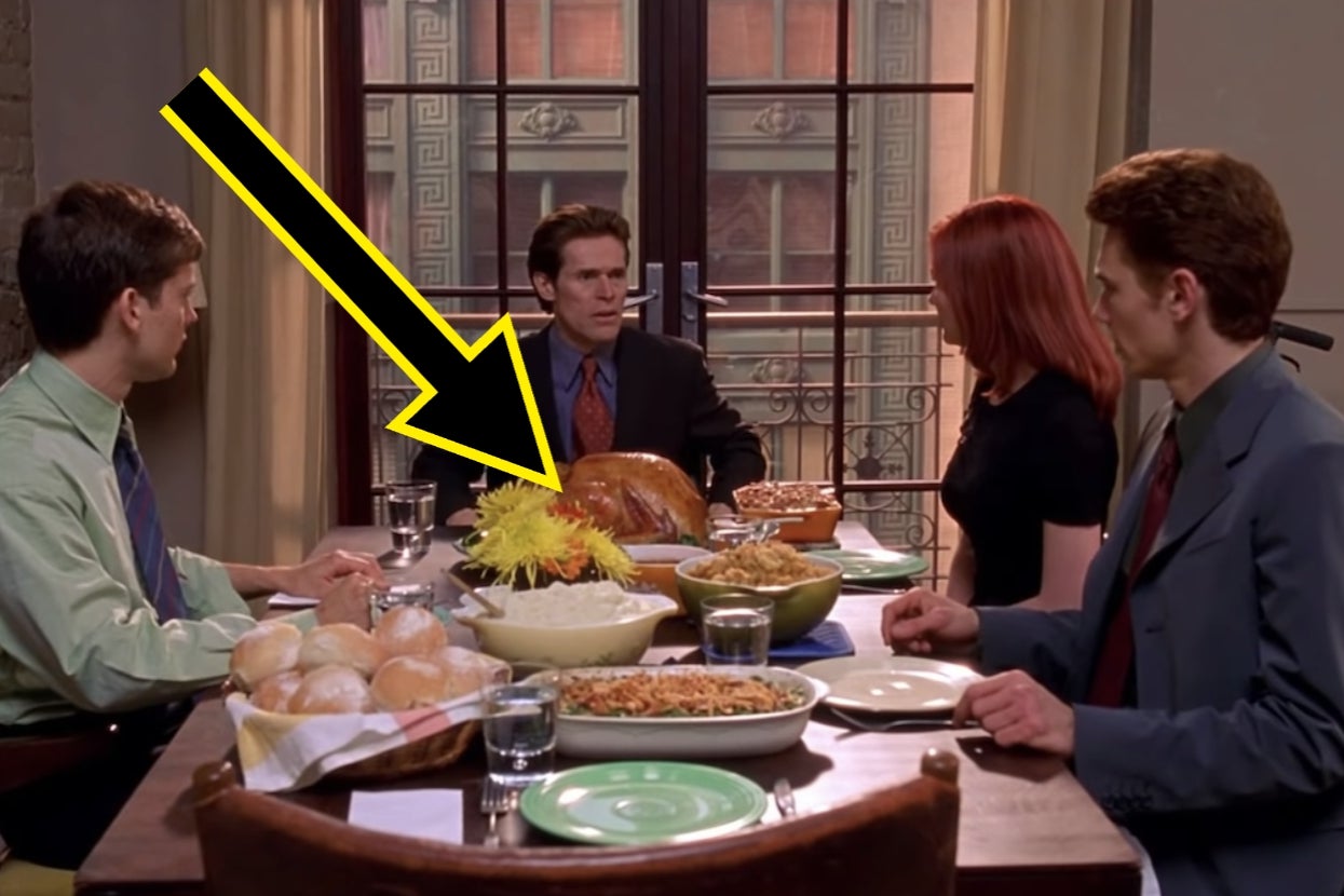 Four people are seated at a dining table with a turkey centerpiece indoors. A large yellow arrow points at one person