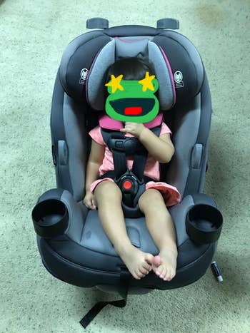 A toddler sits successful a car seat, sucking their thumb, wearing a elemental one-piece outfit