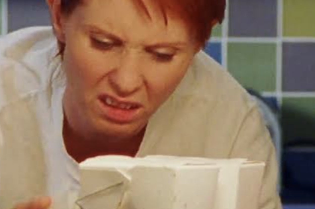 Person with short hair making a confused expression while looking at an incomplete ceramic creation in a studio setting