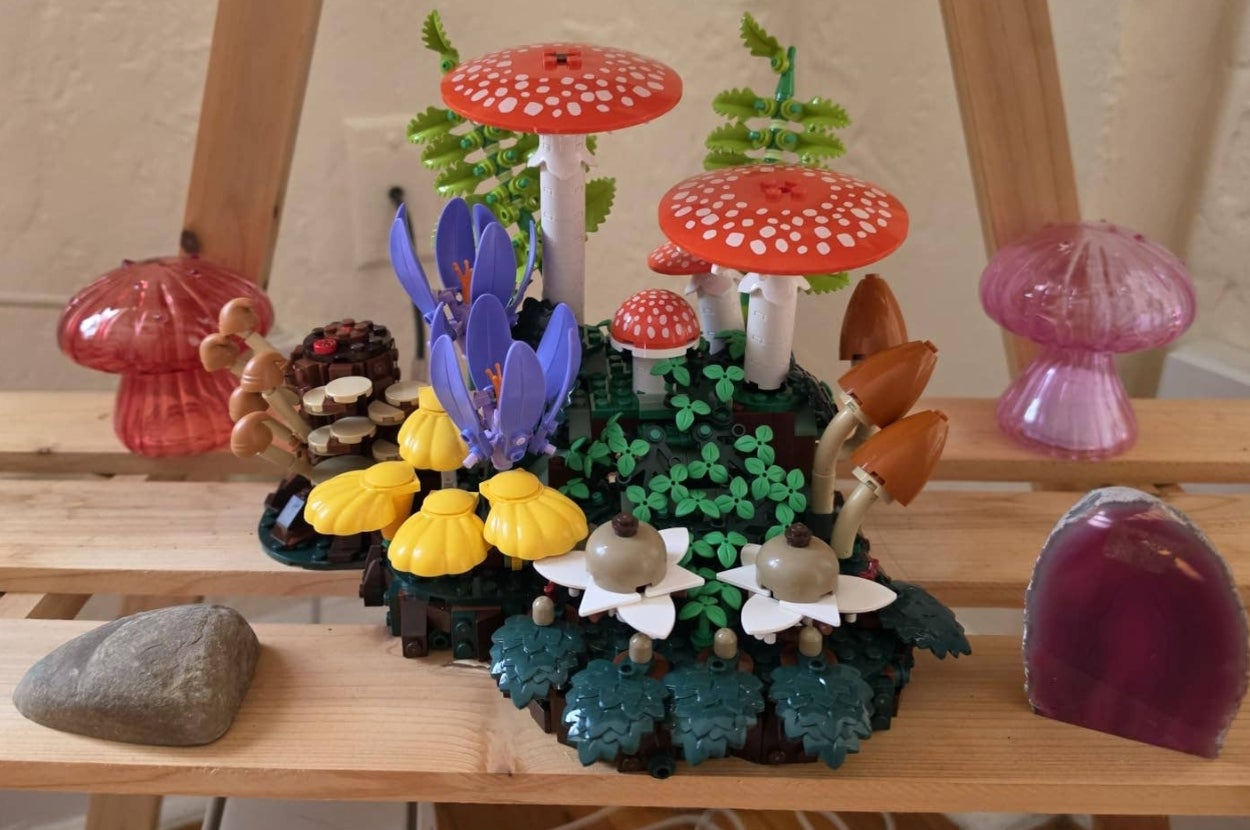 Lego-style mushrooms and plants, including red-capped toadstools and yellow flowers, displayed on a wooden surface with decorative glass pieces