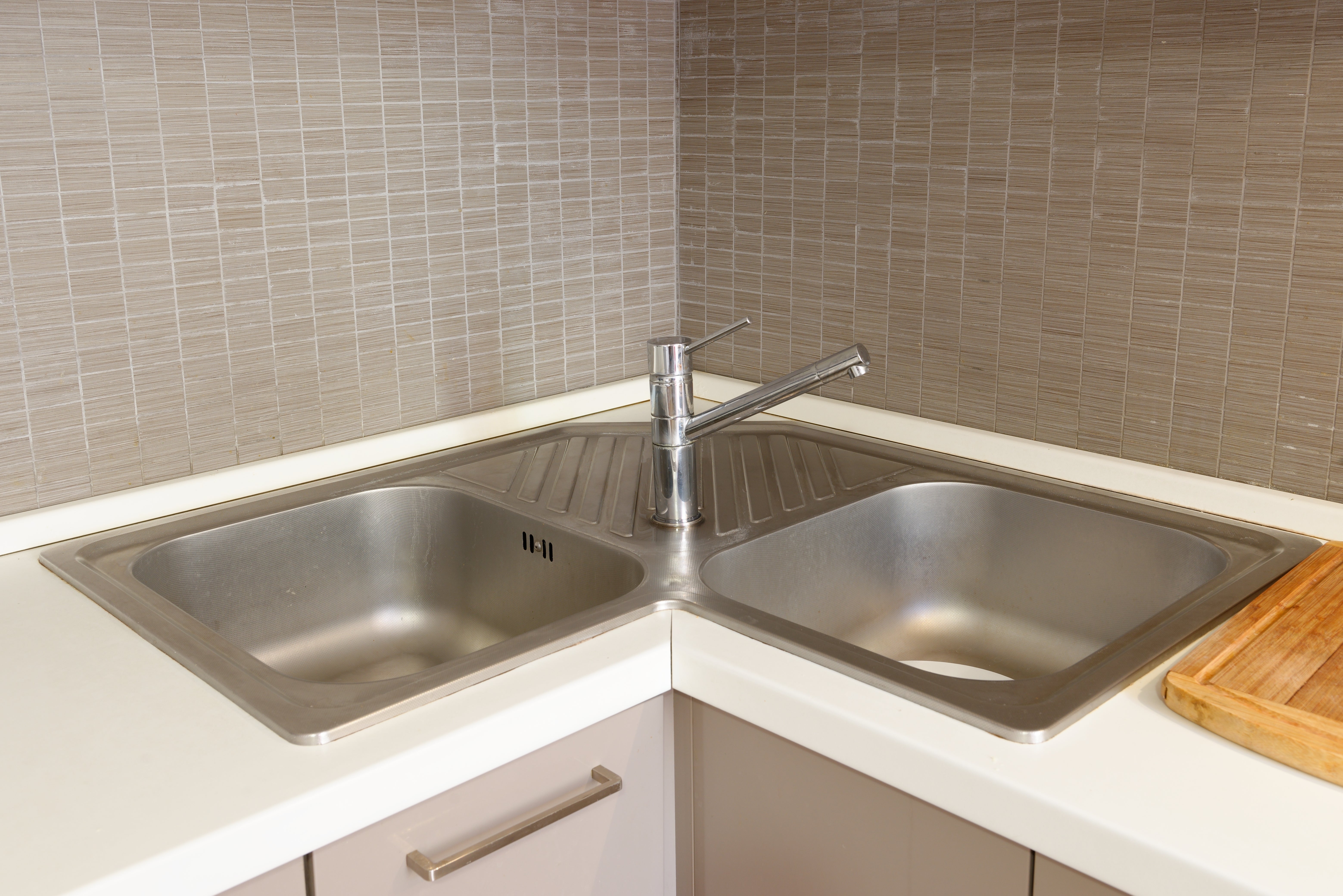 Kitchen corner with a dual-basin sink, modern faucet, tiled backsplash, and a wooden cutting board on the counter