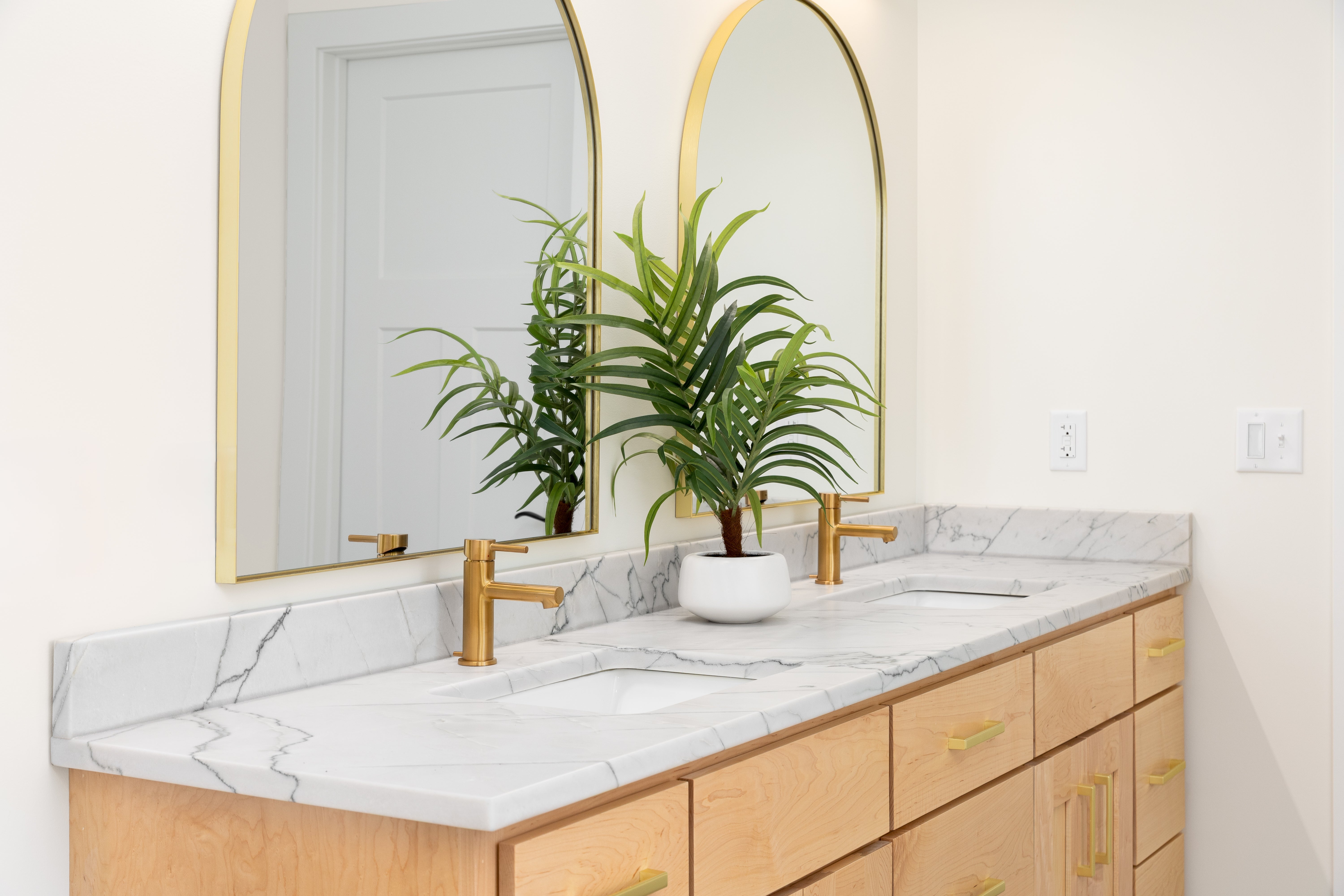 Luxurious bathroom with a marble countertop, gold fixtures, dual sinks, mirrors, and a plant in the center