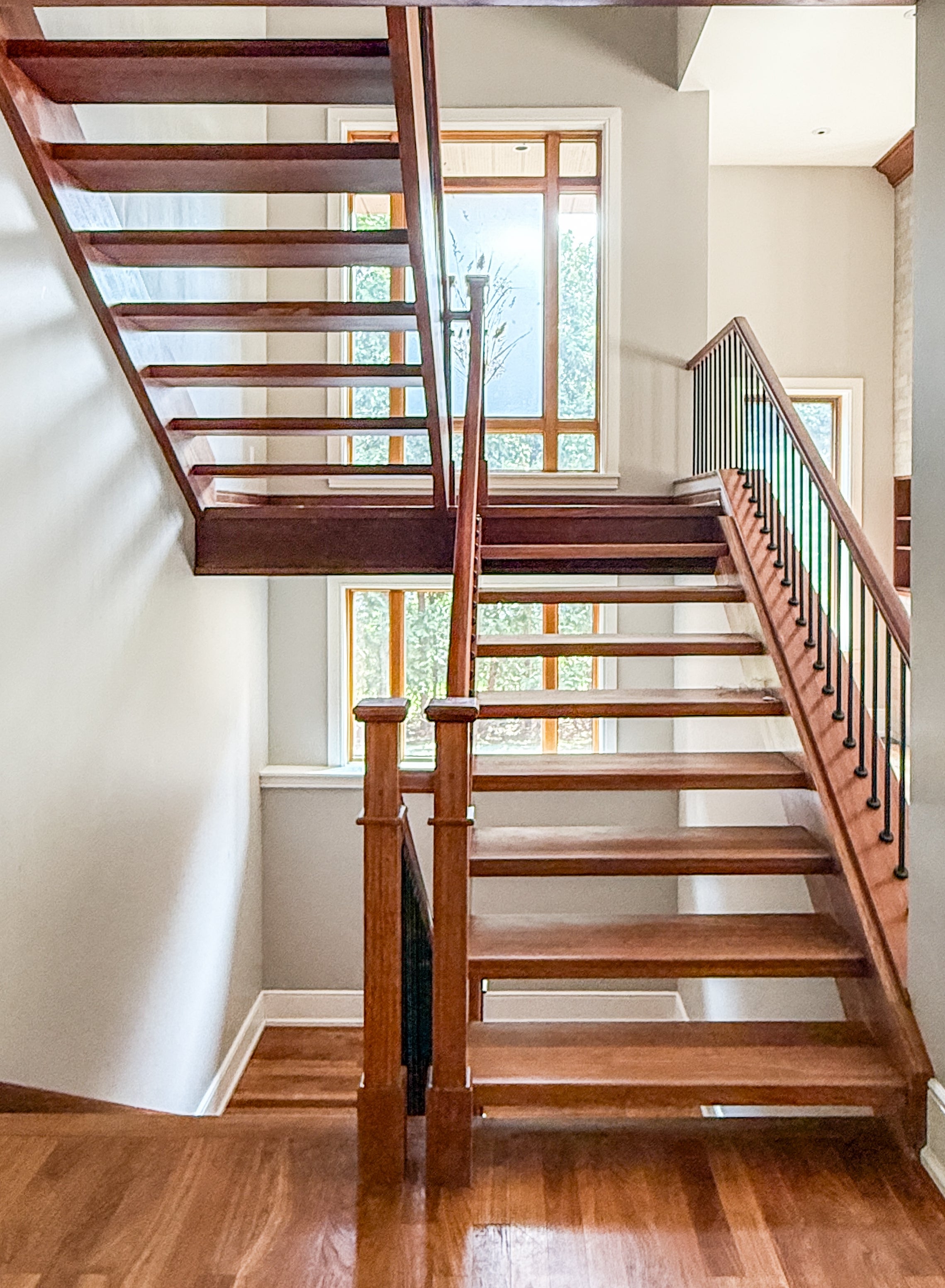 Modern wooden staircase with metal railings, featuring an open design and a window in the background illuminating the space